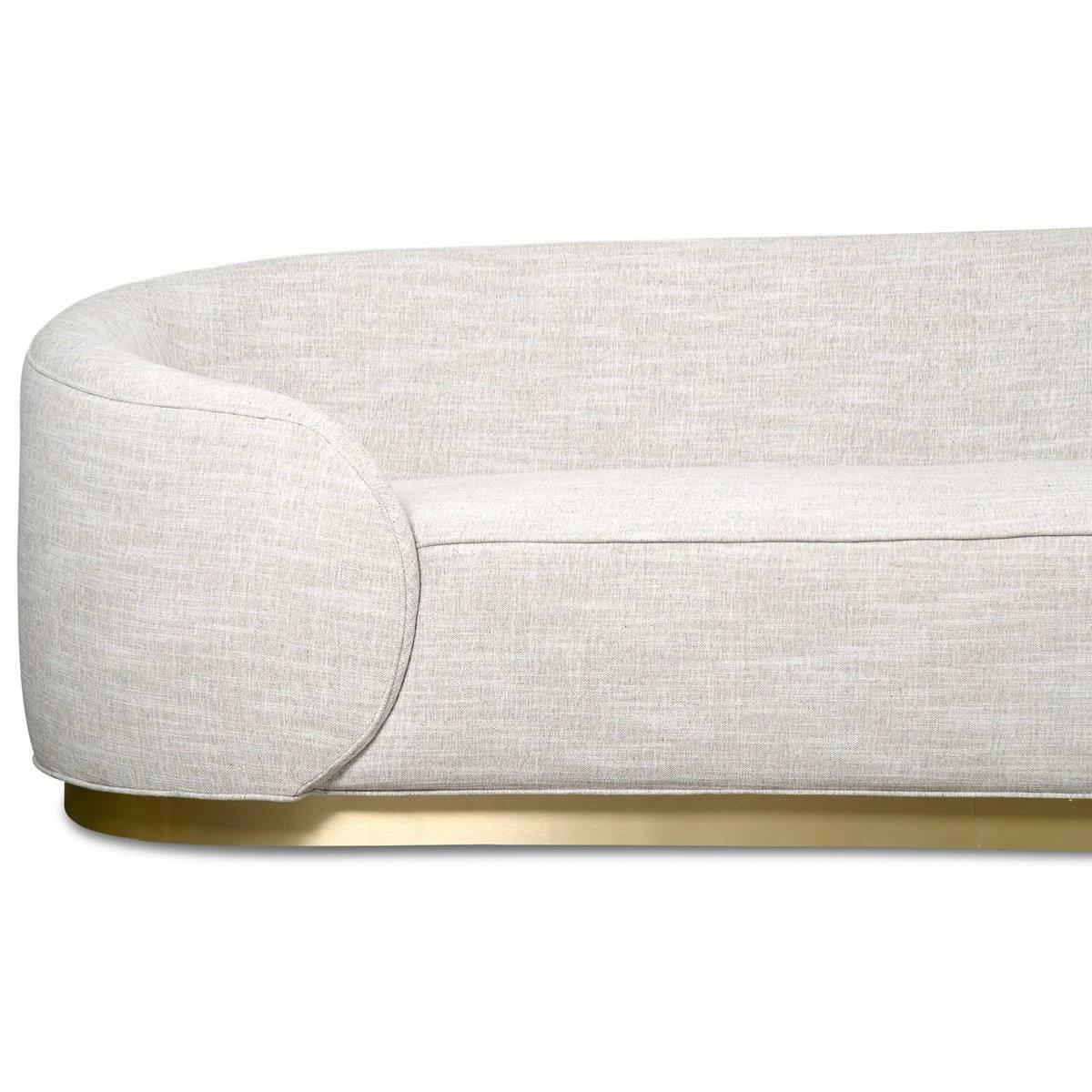 Introducing the Eden Rock sofa in linen. Modern curvy rounded wrap-around arms give a unique look to this bold sofa. The solid natural lines bring serenity and calm to any space. Featuring a customizable brushed brass base and textured tight fitted