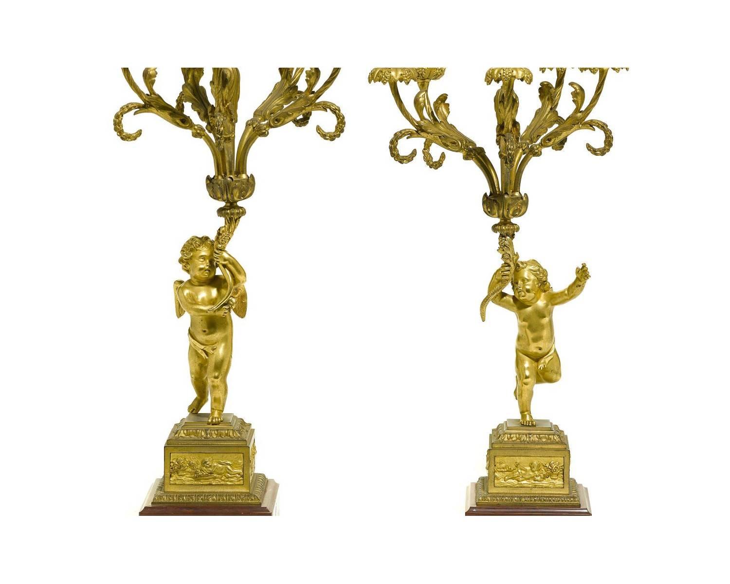 A very fine pair of French 19th century Louis XV style figural gilt bronze and rouge marble six-light candelabra, each with a figure of a standing cherub holding the ornate scrolled arm candelabra, crowned with a gilt bronze candle snuffer in the