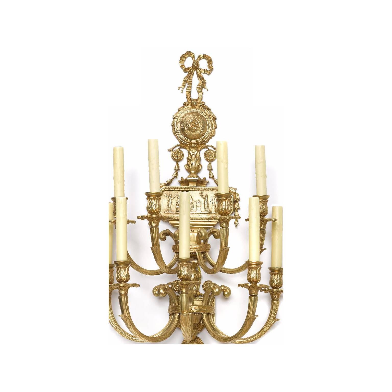 A large pair of neoclassical style gilt bronze eight-light wall lights. The top in the form of a tied bow above a circular rosette. The rectangular back plate with a classical allegorical scene, surmounted with eight scrolled candle arms above a