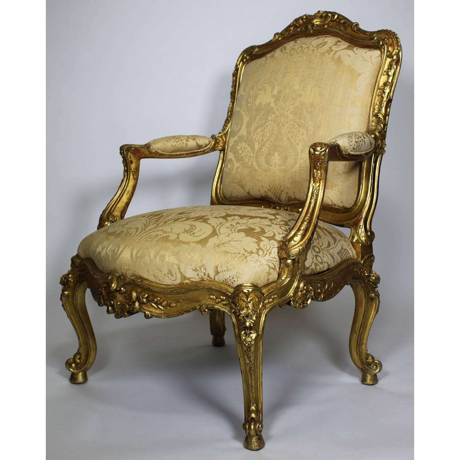 A fine pair of Italian 19th century Rococo style giltwood carved armchairs; the arched upholstered paneled backs with foliate scroll cresting and similar borders, having padded arm supports above slip-in seat, raised on flower heads decorated