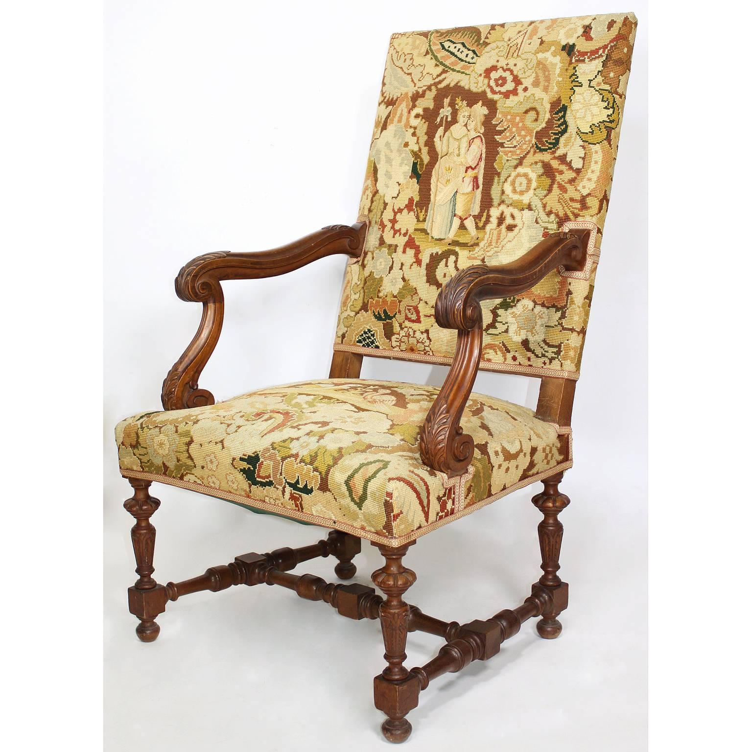 A pair of French 19th-20th century Baroque style carved walnut and needlepoint upholstered hall throne armchairs with raised carved armrests and fluted conjoint legs. The tapestries each depicting romantic courting scenes among trees and a floral