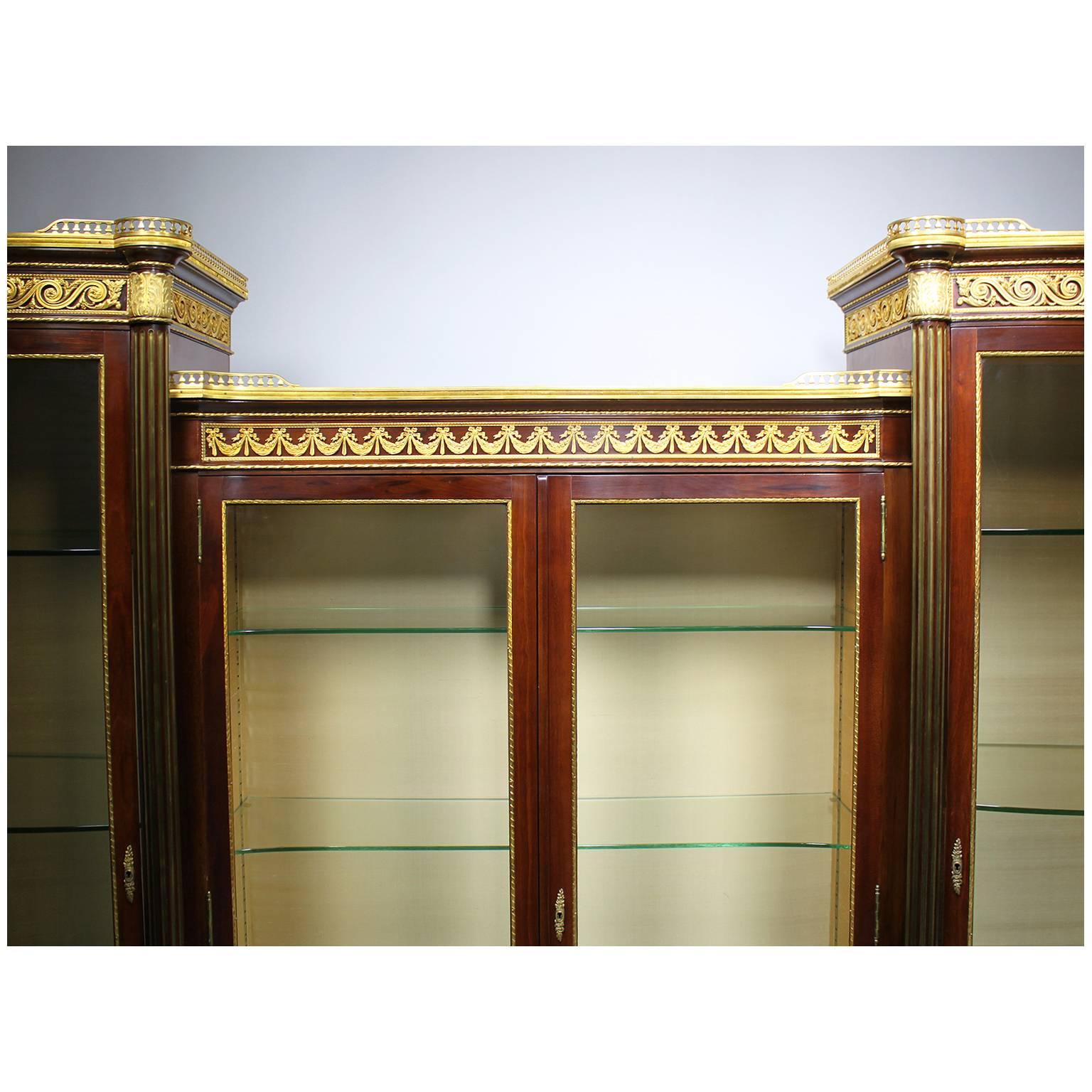 A very Fine French 19th-20th century Louis XVI style mahogany and ormolu-mounted four-door vitrine, with two central bombé glass doors and single bombé glass doors on each side, the fluted mahogany columns with brass inserts and wrapped-around