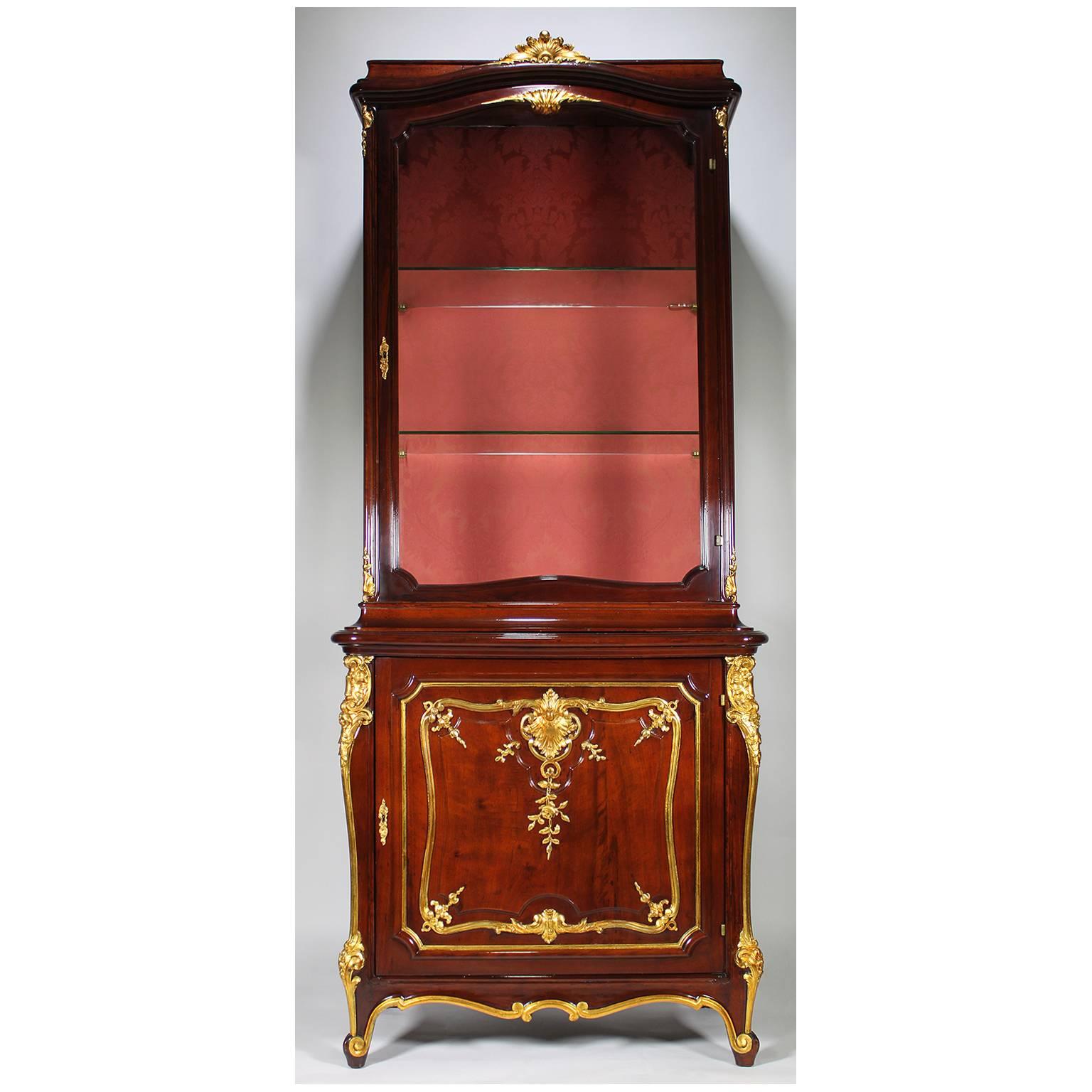 A fine pair of French 19th-20th century Louis XV style mahogany and parcel-gilt-wood carved Vitrines by Mâison de Forest, Paris. Each two-corps cabinet crowned with a carved parcel-giltwood shell above a single door vitrine with two glass shelves.