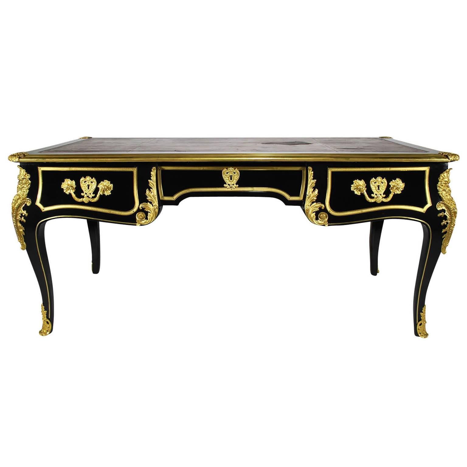 A fine French 19th century Louis XV style ebonized wood and gilt bronze-mounted figural bureau plat (desk) with three drawers and leather top. The shaped rectangular top enclosing a gilt tooled leather writing surface (worn) within a molded border