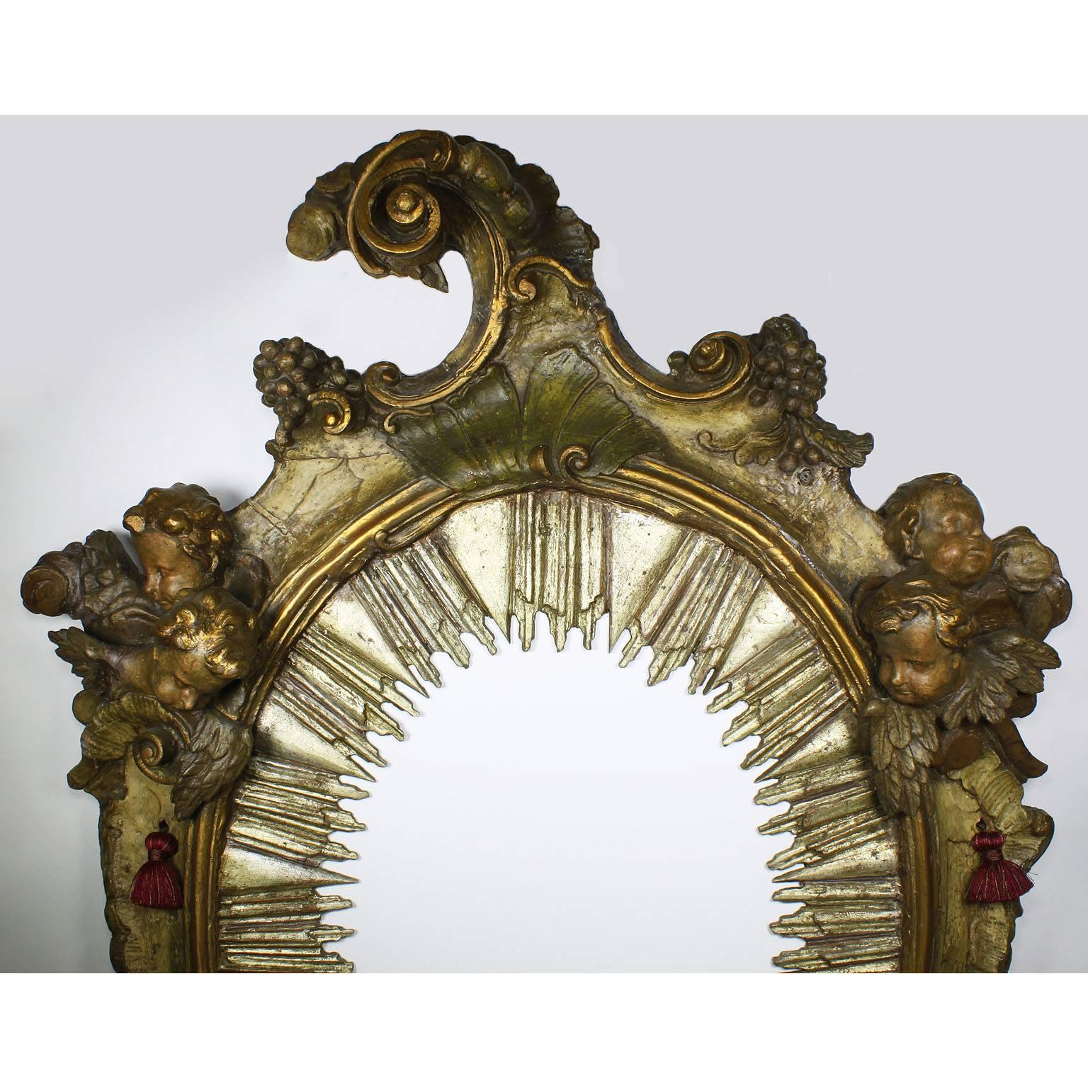 A very fine and palatial Italian Baroque 18th century parcel-gilt and silver carved wood figural mirror, with figures of cherubs, scrolls and acanthus. The ovoid frame crowned with a scrolled cornucopia form finial, surmounted on each side with a