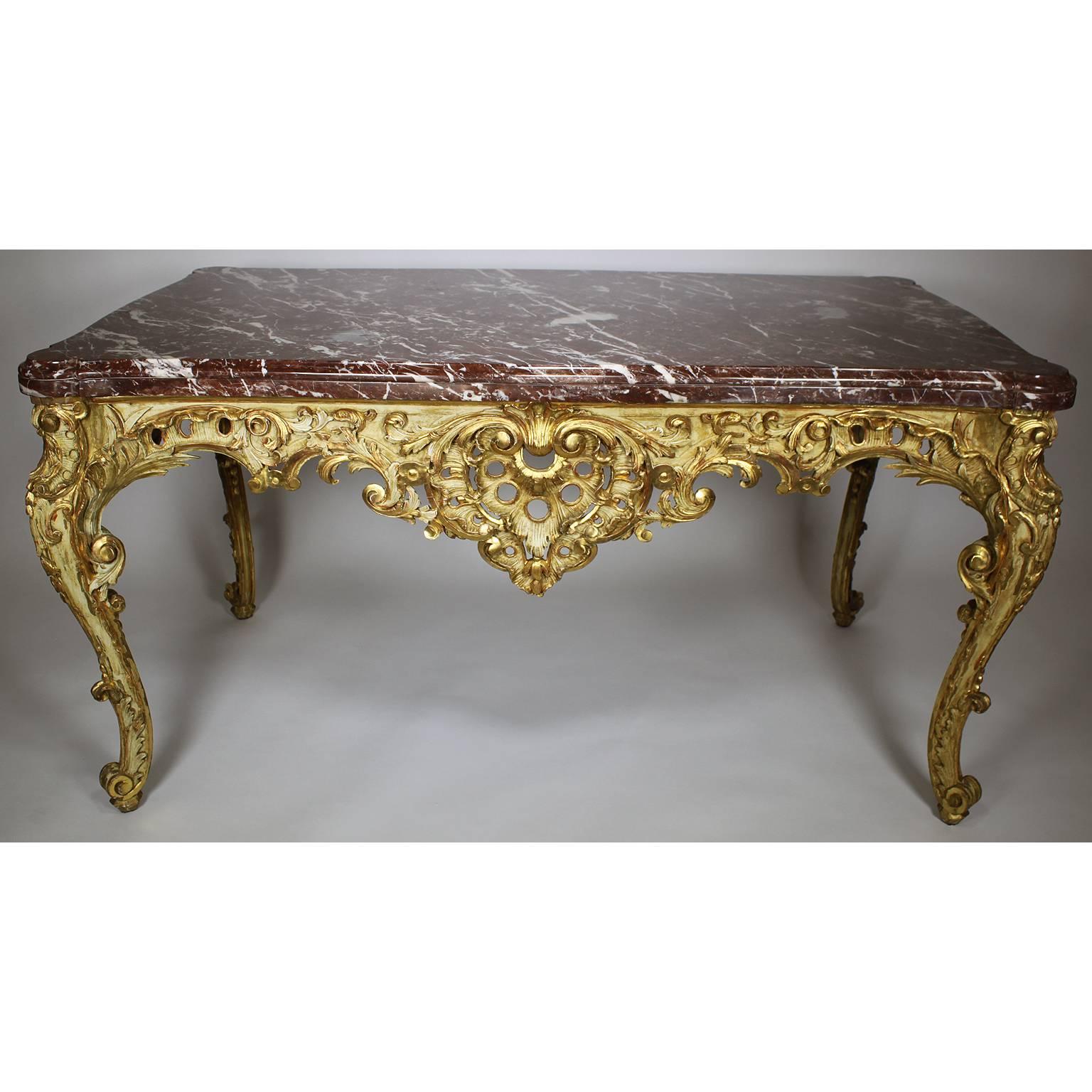 A fine and rare French Rococo Revival 19th century Louis XV style parcel-giltwood carved centre table with marble top. The intricately and partially distressed gilded and cream colored carved apron with scrolls and floral designs, raised on four