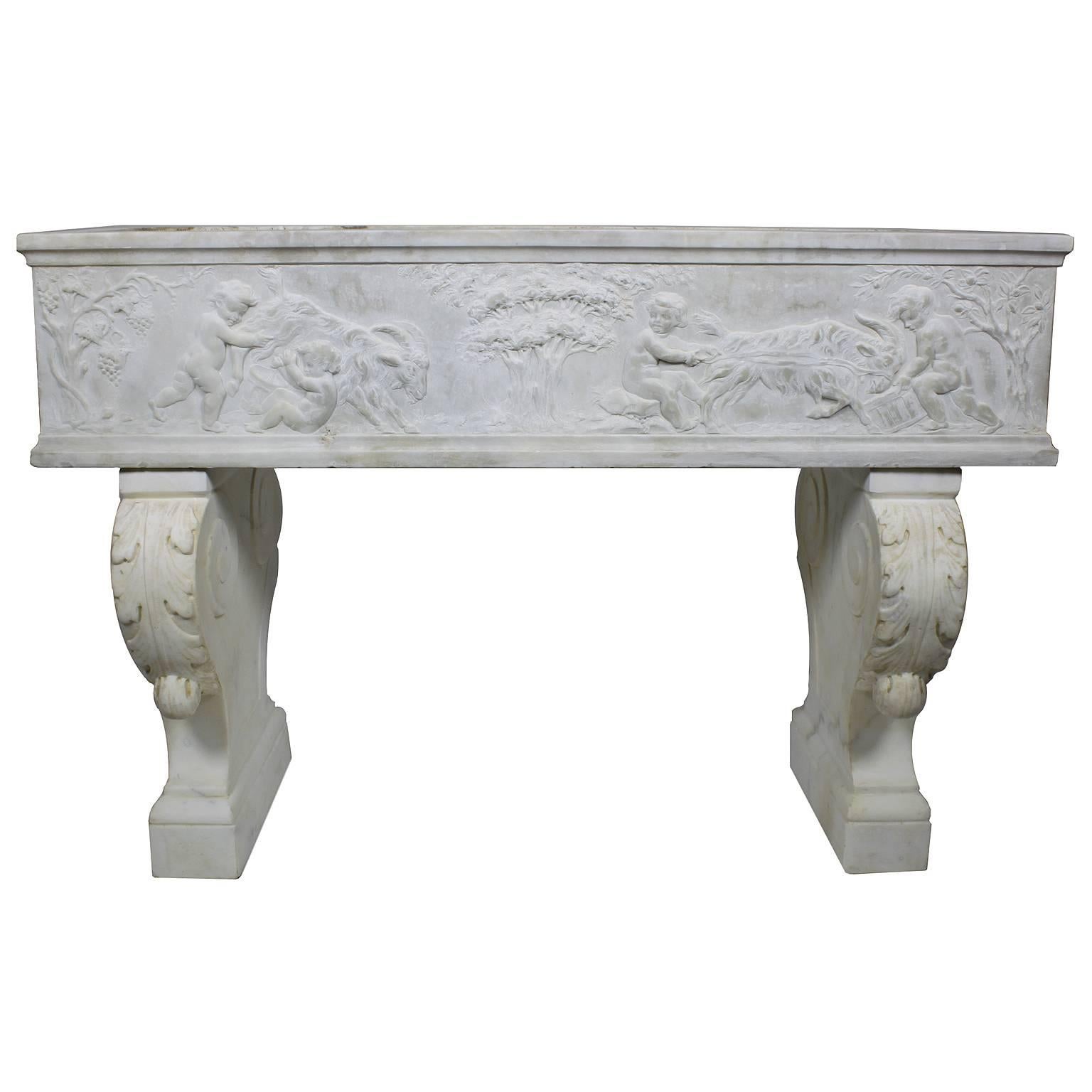 A fine French 19th century whimsical Rococo style white marble carved planter jardinière with figures of playful Putti 'Children' playing with a goats among trees and vines, raised on twin pedestal stands with acanthus leaves, Paris, circa