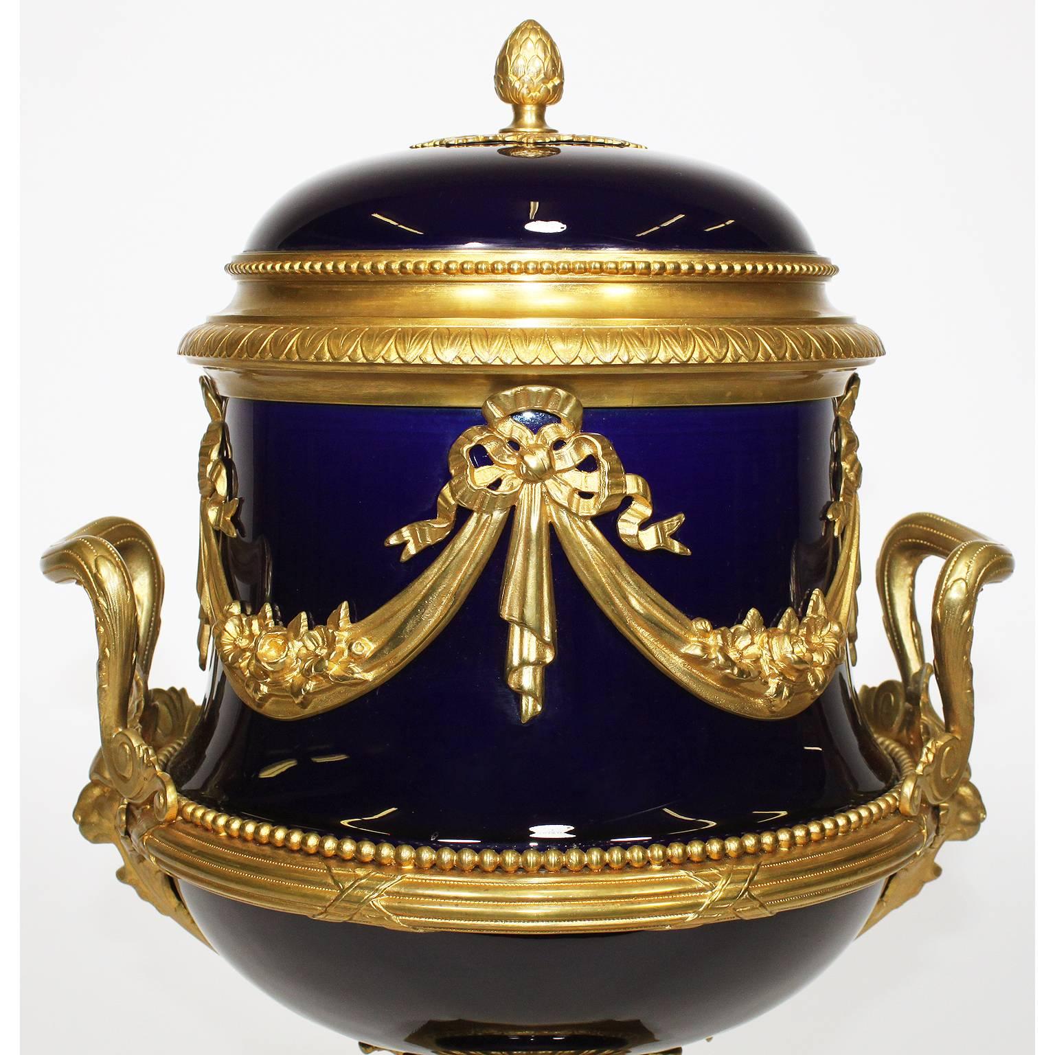 A very fine Napoleon III cobalt blue porcelain and gilt bronze-mounted urn with cover. The trophy shaped urn surmounted with twin scrolled handles, floral tassels tied with ribbons, a banded rim with lion masks, raised on a square gilt-bronze and