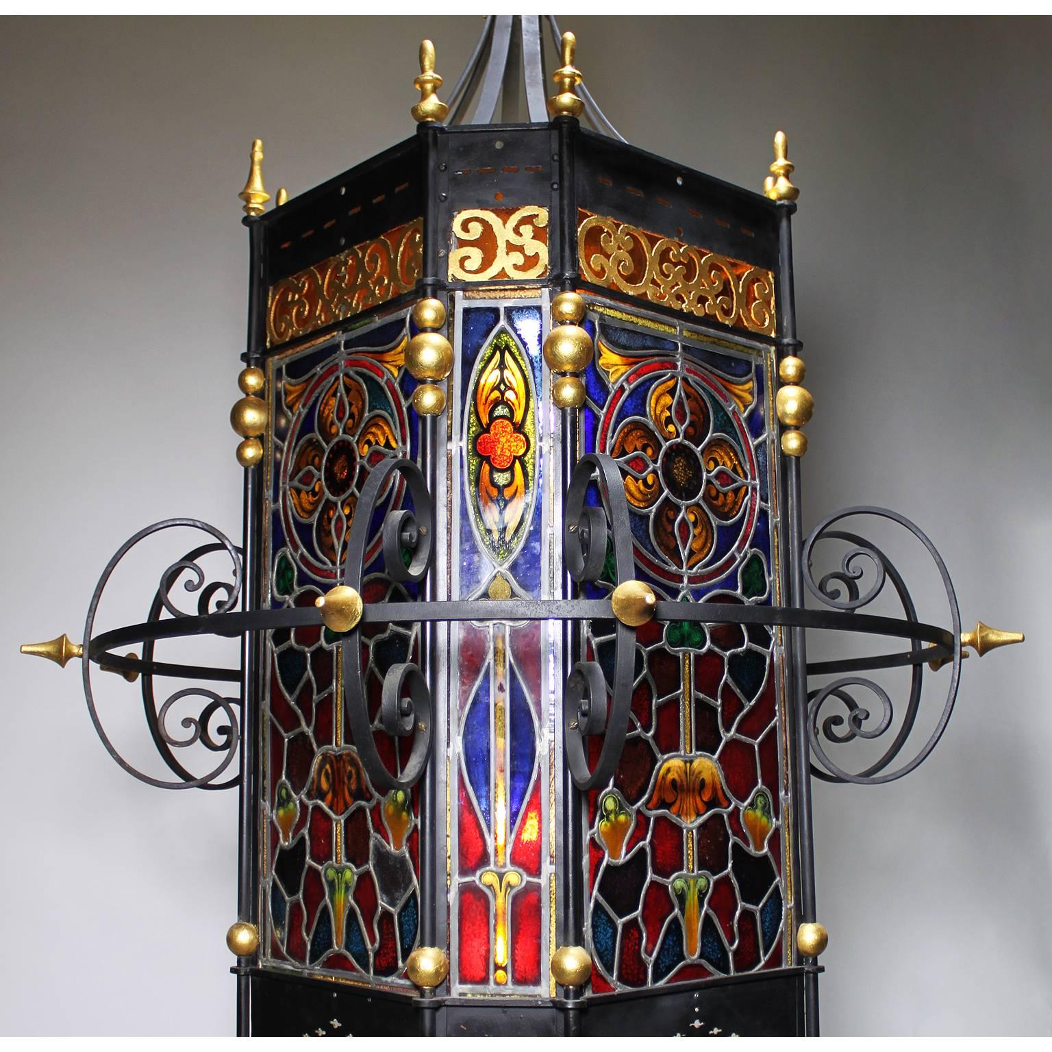 A palatial Italian 19th century Baroque style wrought iron and Vitreaux stain glass paneling entry eight-light grand hall lantern. The square black painted and parcel-gilt iron frame with flat corners, surmounted with a circular and a scrolled