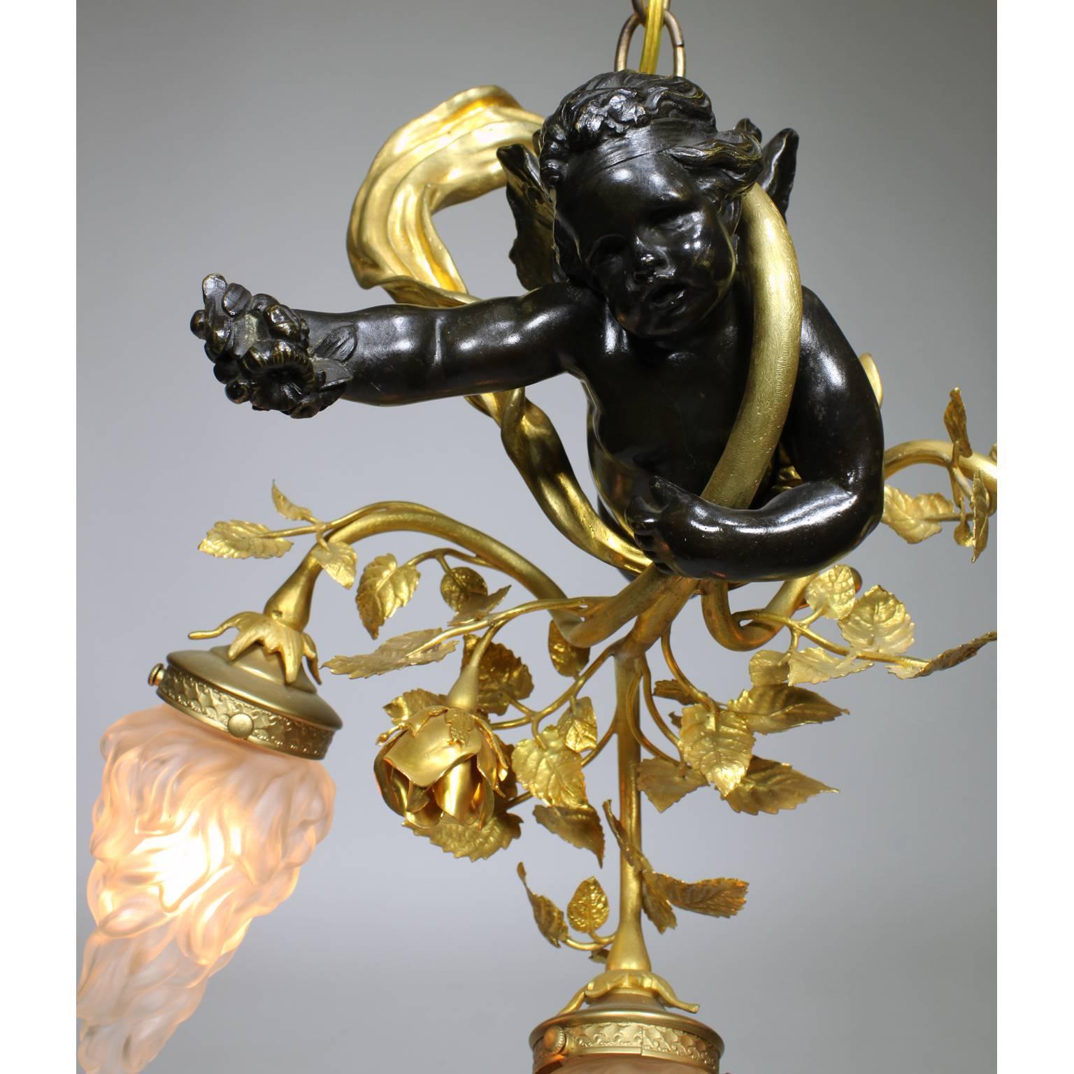 Une belle suspension de lustre Belle Époque française du 19-20e siècle à trois lumières en bronze patiné, doré et métal doré. La figure en bronze patiné foncé d'un chérubin planant s'enroulant autour d'un ruban en bronze doré soufflant tout en