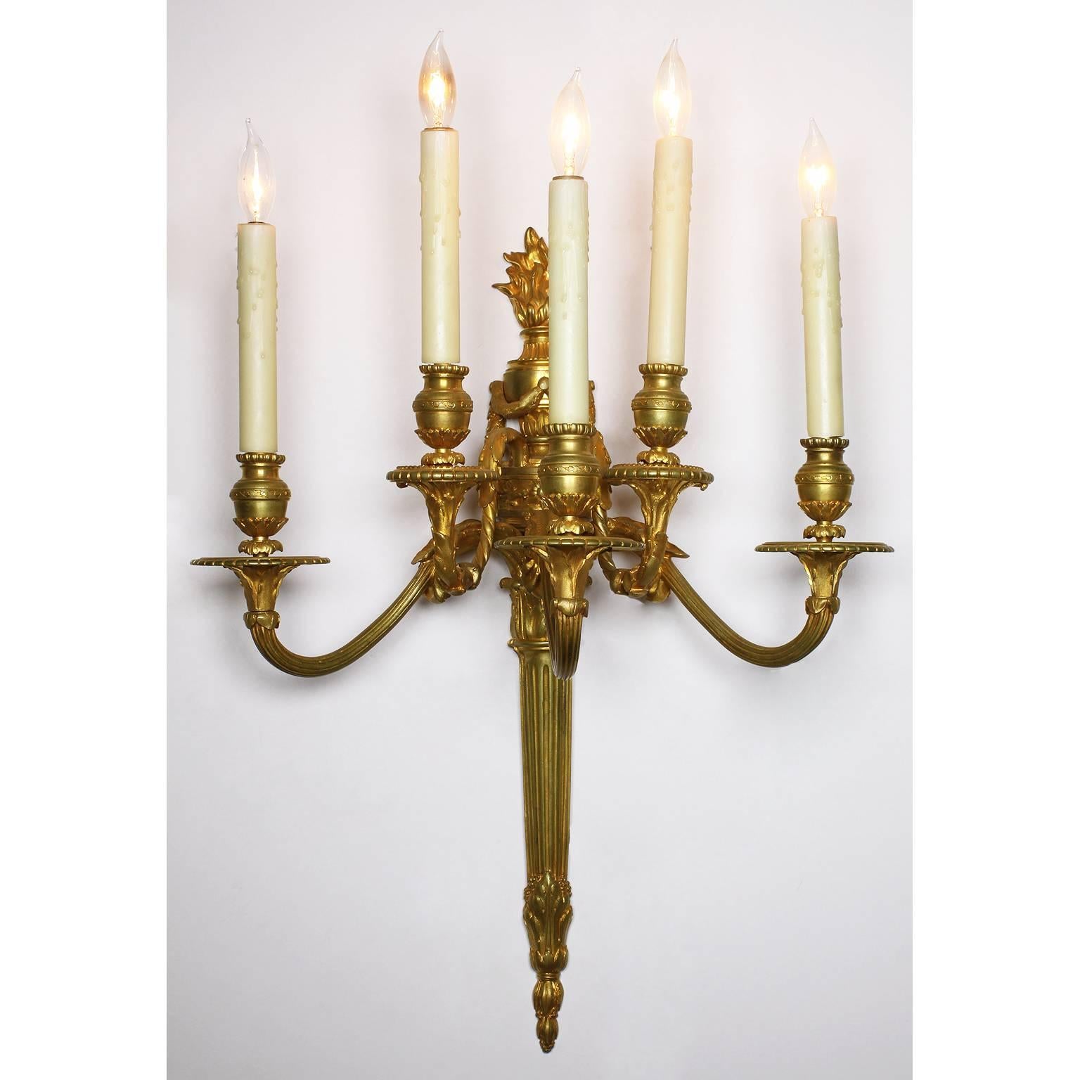 Paire d'appliques murales à cinq lumières en bronze doré de style Louis XVI du XIXe siècle. Chaque lumière a des bras en volutes et est couronnée d'une urne néoclassique surmontée de couronnes et surmontée d'une flamme brûlante. Estampillé des