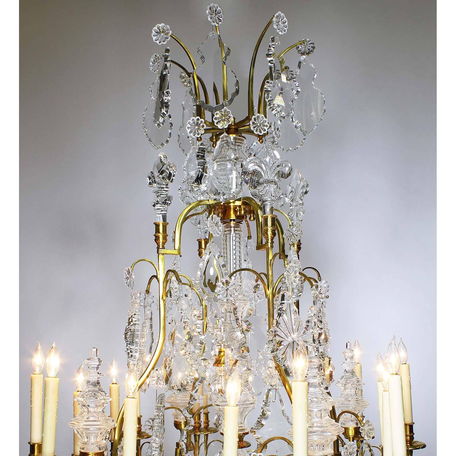 Paire de lustres à seize lumières en bronze doré et verre taillé de style Louis XV. Les montures en bronze massif sont surmontées de pendentifs, de tours moulurées, de fleurs de lys et d'un support central, à la manière de Baccarat. vers le 20e