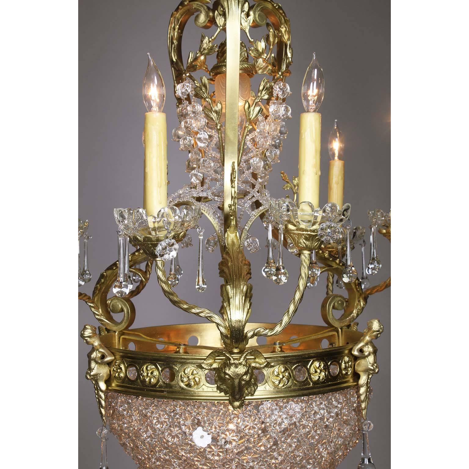 A French Belle Époque gilt bronze and cut-glass six-arm figural basket chandelier. The elongated gilt-bronze frame with six candle-arms with glass wax-drip plates, surmouted with interlaced molded cut-glass flowers, cast bronze figures of