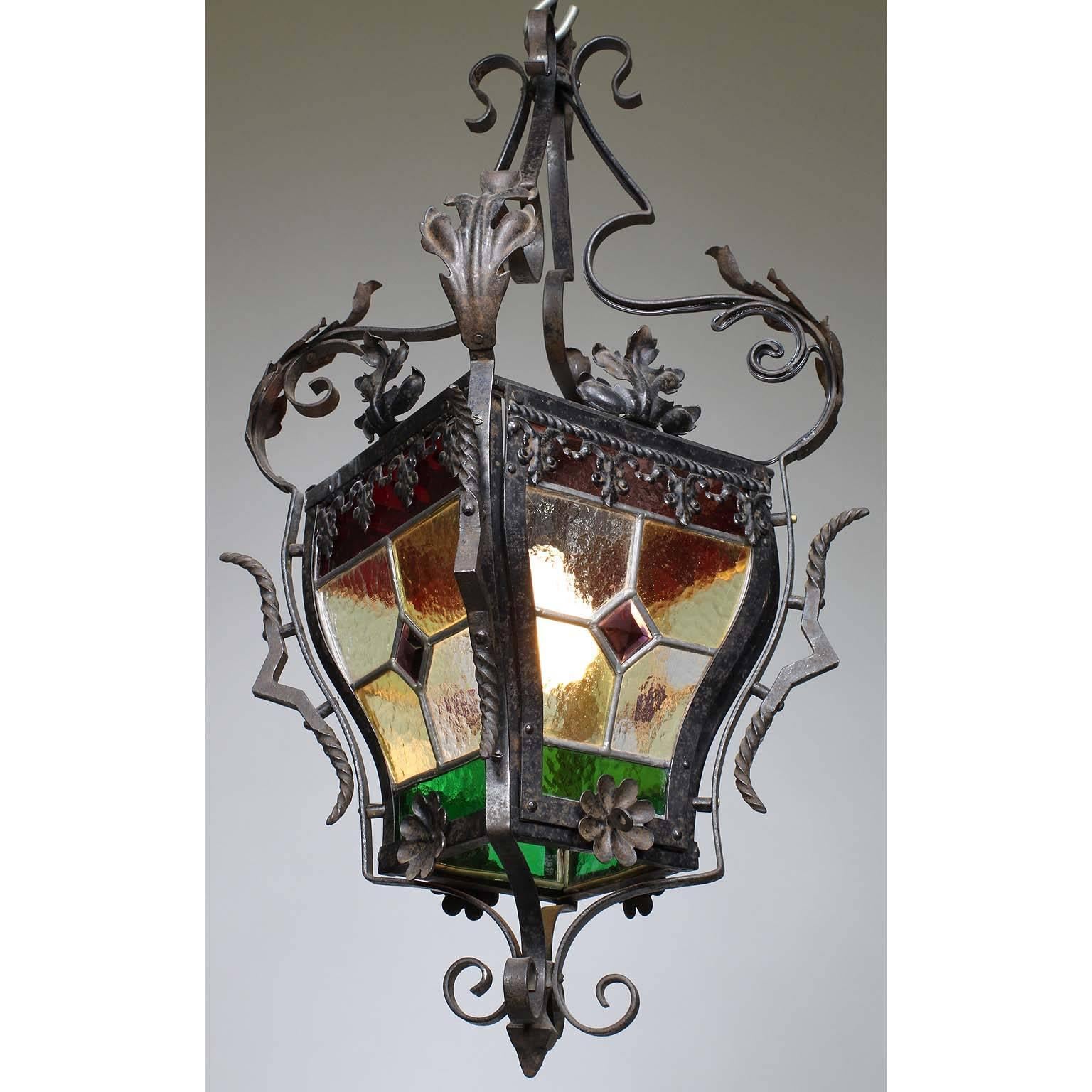 A French 19th-20th century Baroque Revival style wrought iron and four-color vitreaux stained glass single-light hall lantern, the rounded four stained glass panels with red, green, opaque and burgundy glass work, the scrolled wrought iron body