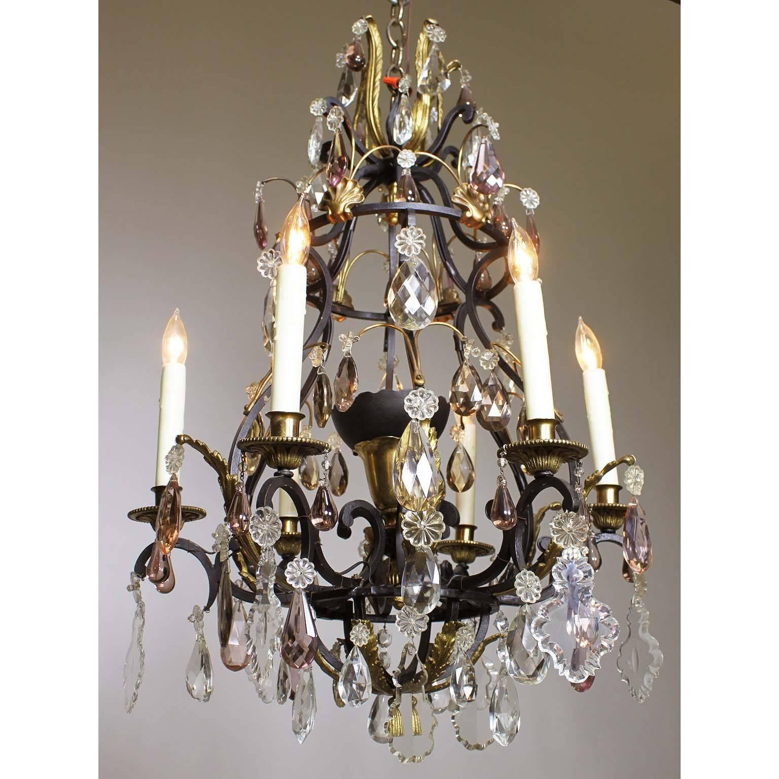 A French 19th-20th century Louis XV style wrought iron and bronze seven-light color crystal (cut-glass) chandelier. The black painted iron frame with six candle arms and a center light inside a cups, some of the pendants and drops are in amethyst