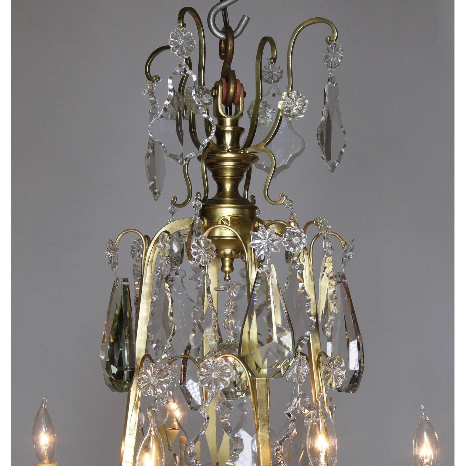 Lustre à neuf lumières en bronze doré et verre taillé de style Louis XV. Le corps allongé avec des pendentifs en verre taillé (cristal) surmontés de huit bras de bougie et d'un abat-jour central en verre dépoli, vers 1900.

Mesures : Hauteur : 44