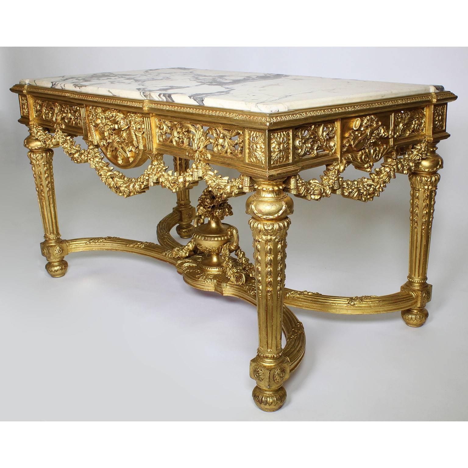 A fine French 19th-20th century Louis XVI style giltwood carved centre hall table. The rectangular shaped intricately carved frame with an X-stretcher centre with a urn, all surmounted with floral swaged garlands and wreaths with tassels,