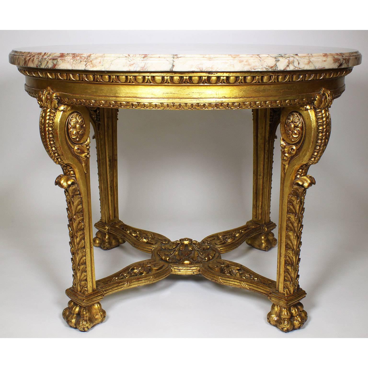 A French Baroque 19th-20th century Louis XV/XVI Transitional Style Gildwood Carved Circular Center Table with a Veined Peach Colored Brocatelle Marble Top, the four legs each with carvings of scrolls and acanthus ending on lion-claws, all joined by