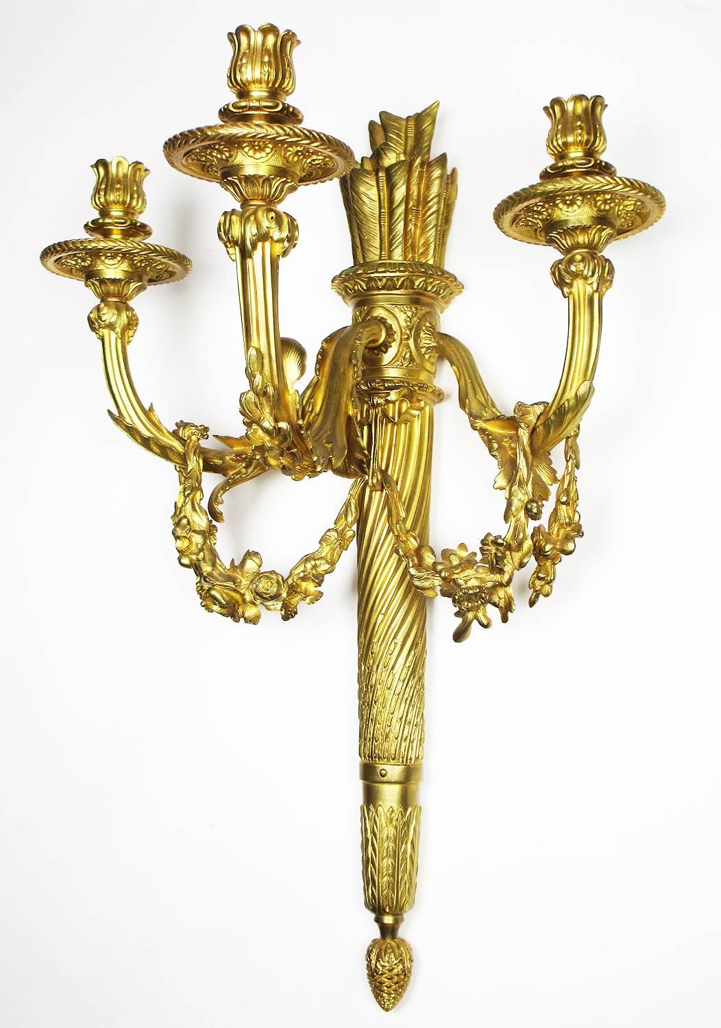 A very fine pair of French 19th-20th century Louis XVI style gilt bronze three-light wall sconces in the form of torches with flower swags over each candle-arm, circa 1900, Paris.

Height: 23 inches (58.4 cm).
Width: 16 1/2 inches (41.9