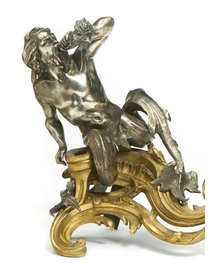 A fine pair of French 19th century Louis XV style figural gilt bronze and silver plated bronze chenets, each surmounted by a triton blowing a seashell Horn, resting on a pierced rocaille gilt bronze base. Stamped 