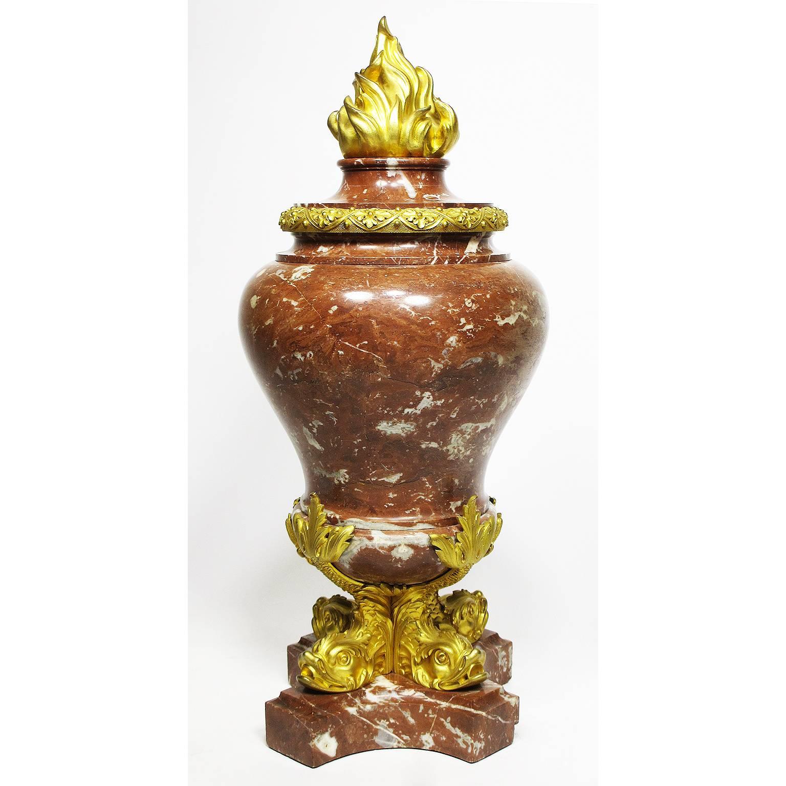 A fine pair of French 19th century Rouge-Royal marble and figural gilt bronze-mounted flambeaux urns surmounted with four ormolu figures of dolphins supporting the center urn with their upright tails and crowned with an ormolu burning flame, Paris,