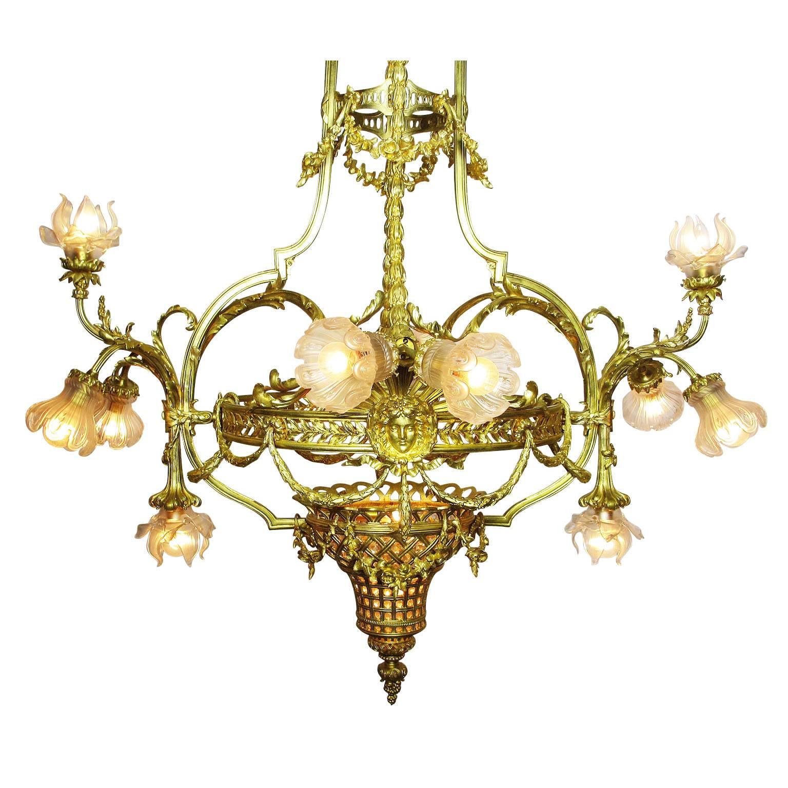 Ein sehr feiner und großer französischer Belle Epoque 19./20. Jahrhundert Louis XIV Stil Zwölf-Licht Gold-Bronze Figural Kronleuchter mit mattierten Glasschirmen. Der eiförmige Korpus mit verschnörkeltem Akanthuskranz trägt ein Medaillon, das Ludwig