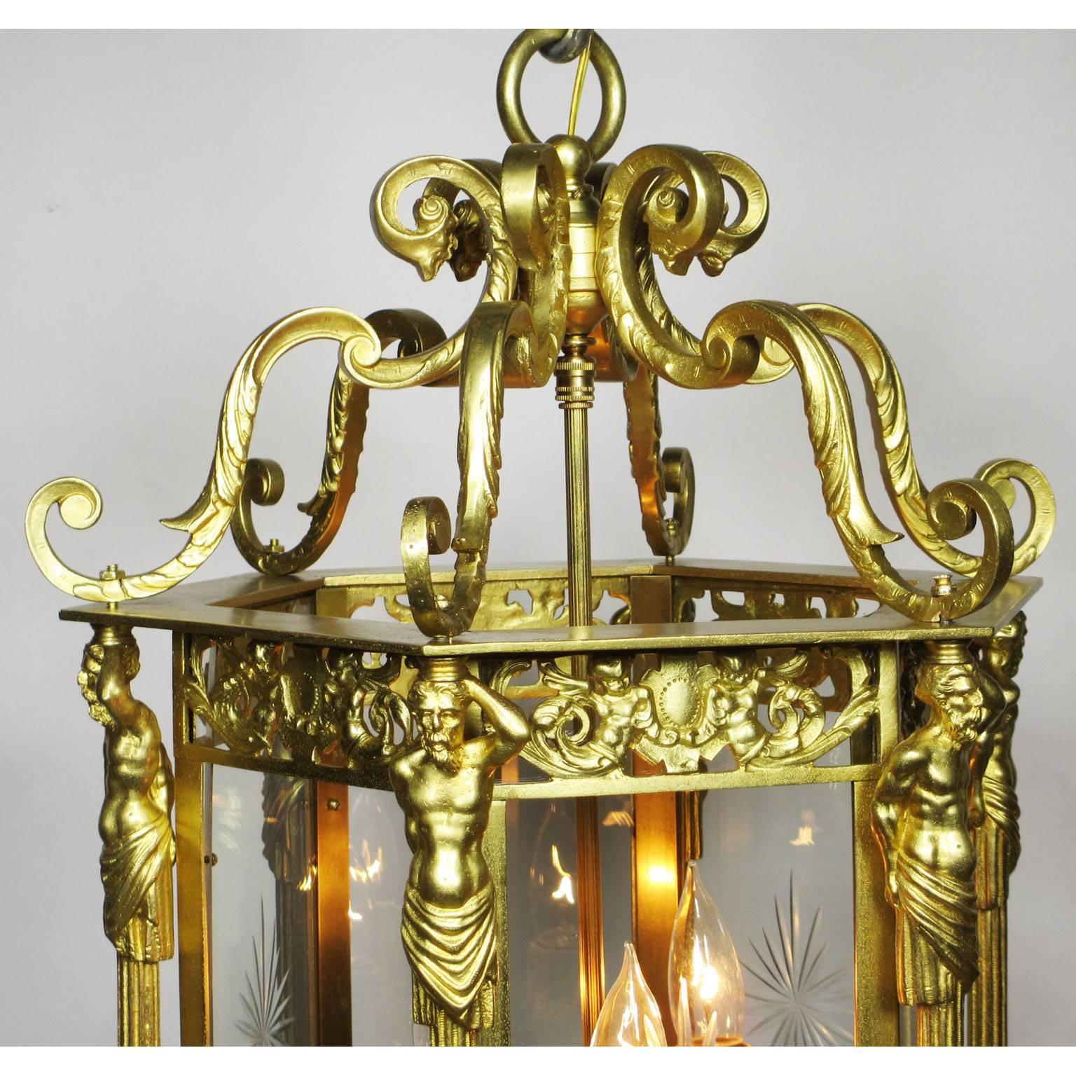 An English 19th-20th century neoclassical style figural hexagonal three-light gilt bronze lantern with figures of bearded male caryatids and winged gargoyles, every other glass panel centered with an edged glass starburst, possibly supplied by