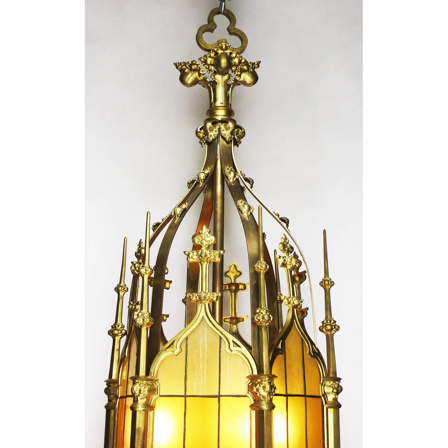 A very fine and large set of four French 19th-20th century Gothic Revival style gilt bronze and glass six-light hanging lanterns with opaque-yellow stained-art glass, the top crowned with a cluster of fruits, circa 1900.

Note: These are a set of