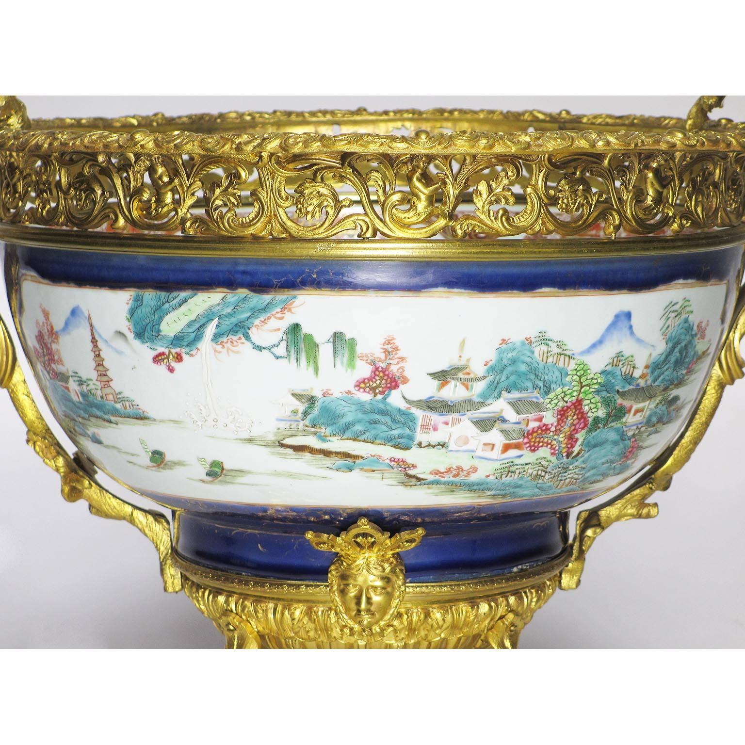 A very fine and large 19th century Chinese porcelain and French figural ormolu-mounted Chinoiserie style centerpiece. The circular ovoid bowl, maybe 18th century Jiaqing period (unverified), decorated with pagodas and landscape scenes, flanking