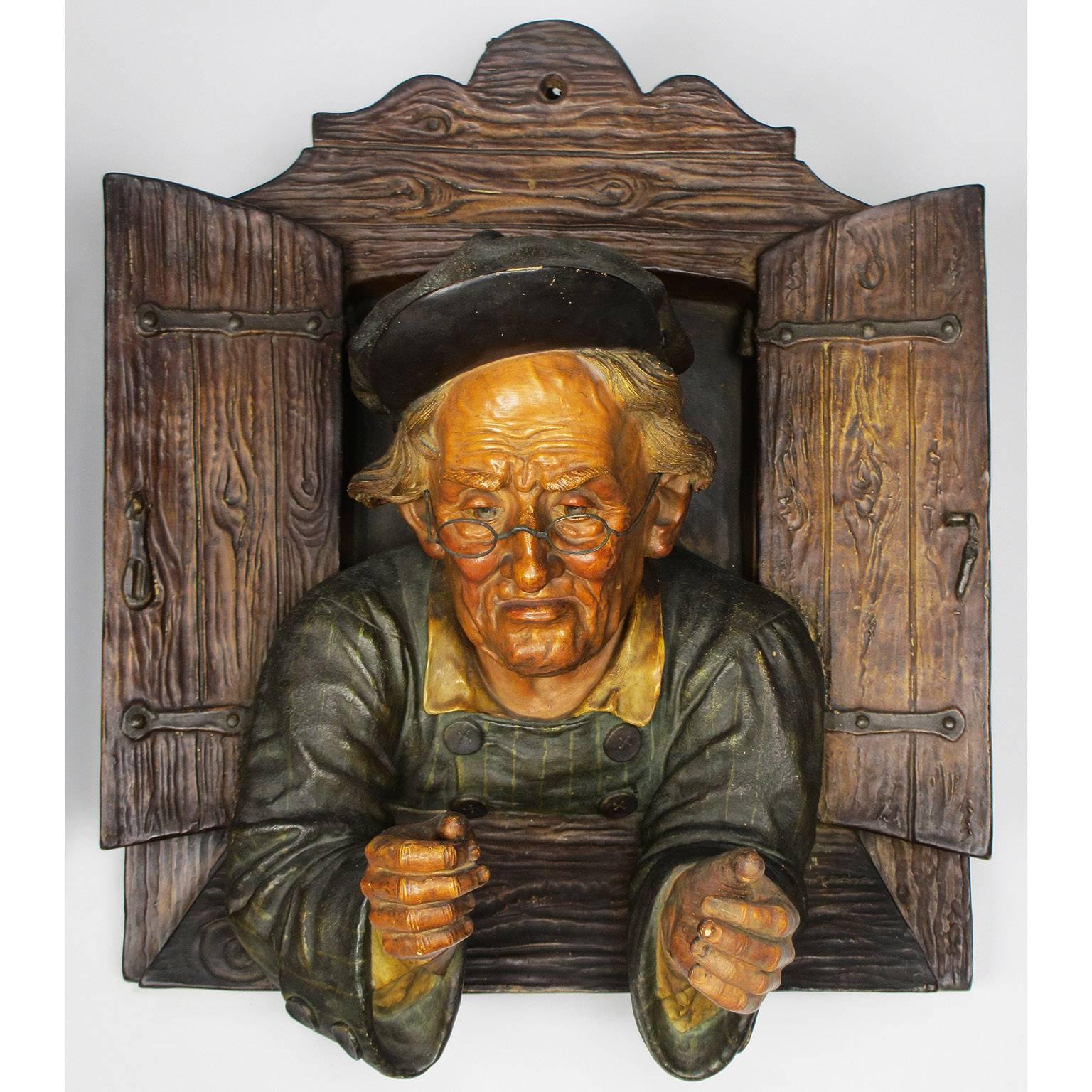 A fine and charming pair of Austrian 19th century polychromed majolica hanging wall sculptures of an elderly couple peeking through a window, probably by Friedrich Goldscheider (Goldscheider'sche Porzellan-Manufactur und Majolica-Fabrik.) Each wall