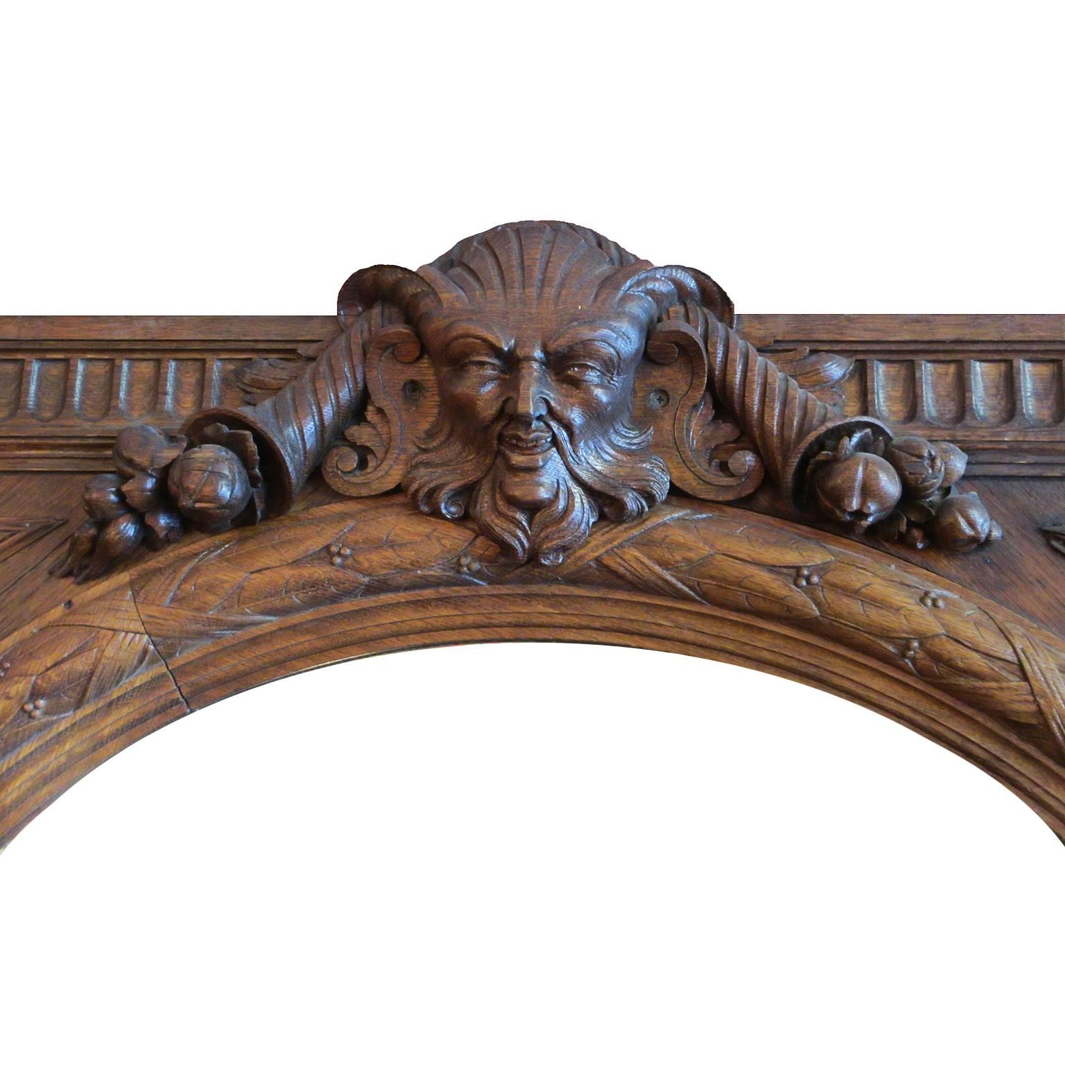 Italian Renaissance revival style 19th century carved oak figural mirror frame with a circular beveled mirror plate. The square shaped body with arrowhead corners, crowned with a carved allegorical mask of a bearded god flanked with cornucopias