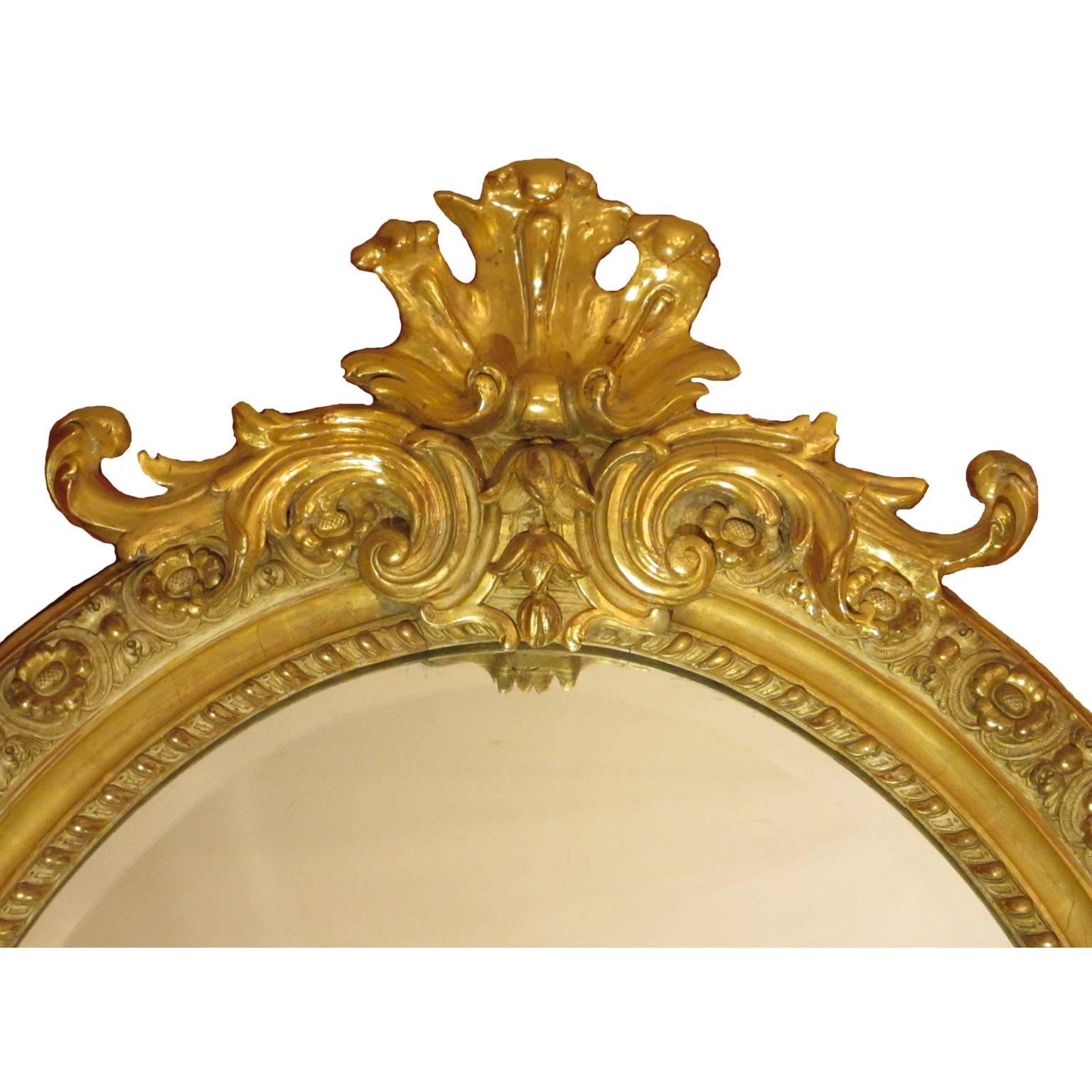 A fine and large French 19th century Louis XVI style giltwood and gesso carved oval mirror frame with a beveled glass plate. All gilding original. The ornately decorated frame with a floral design and crowned with a scrolled and acanthus leaves