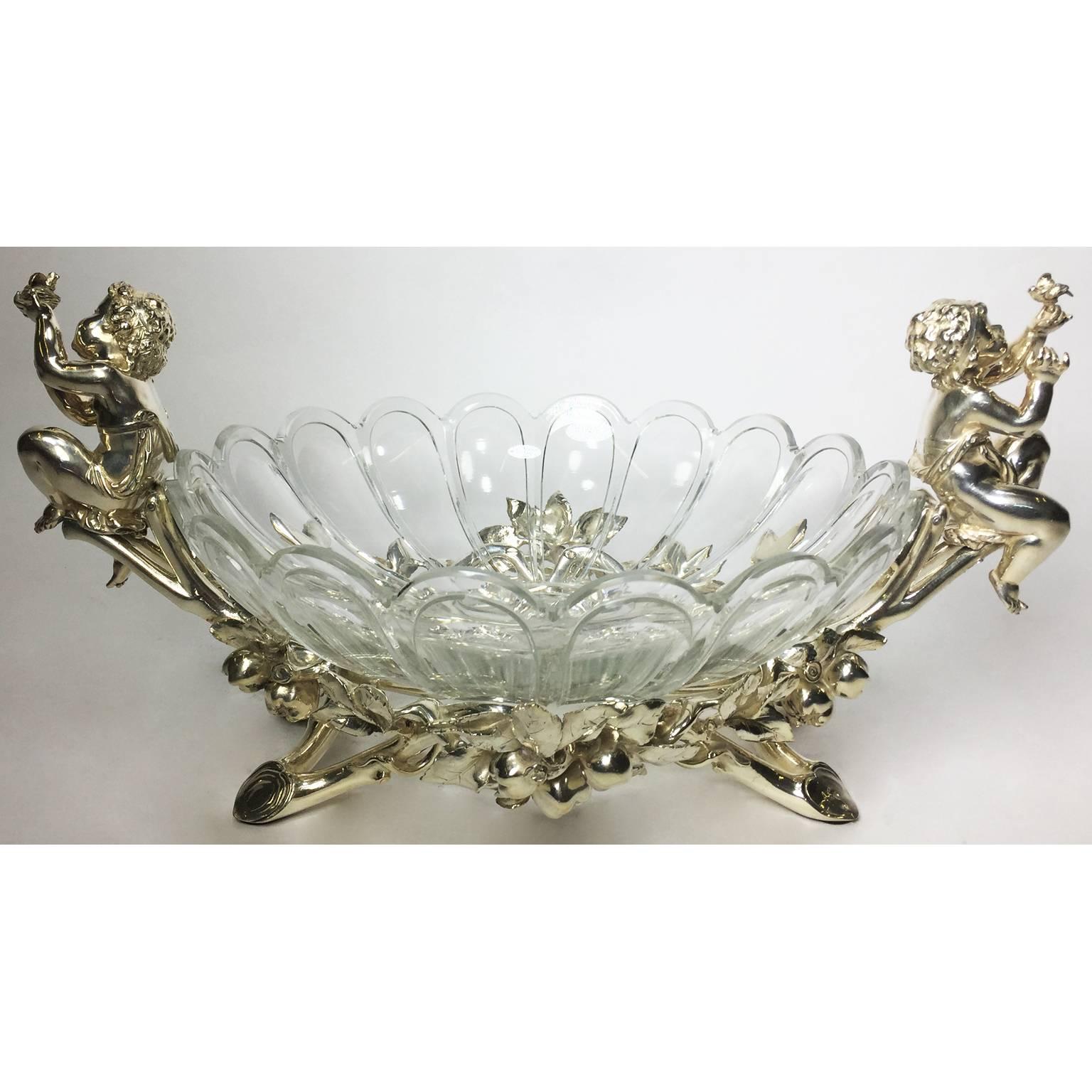 A very fine French 19th-20th century Christofle & Cie Louis XV style silvered figural centerpiece with a circular scalloped cut-glass bowl attributed to Baccarat, the center-dish flanked by two seated putti, one holding a bird and the other a