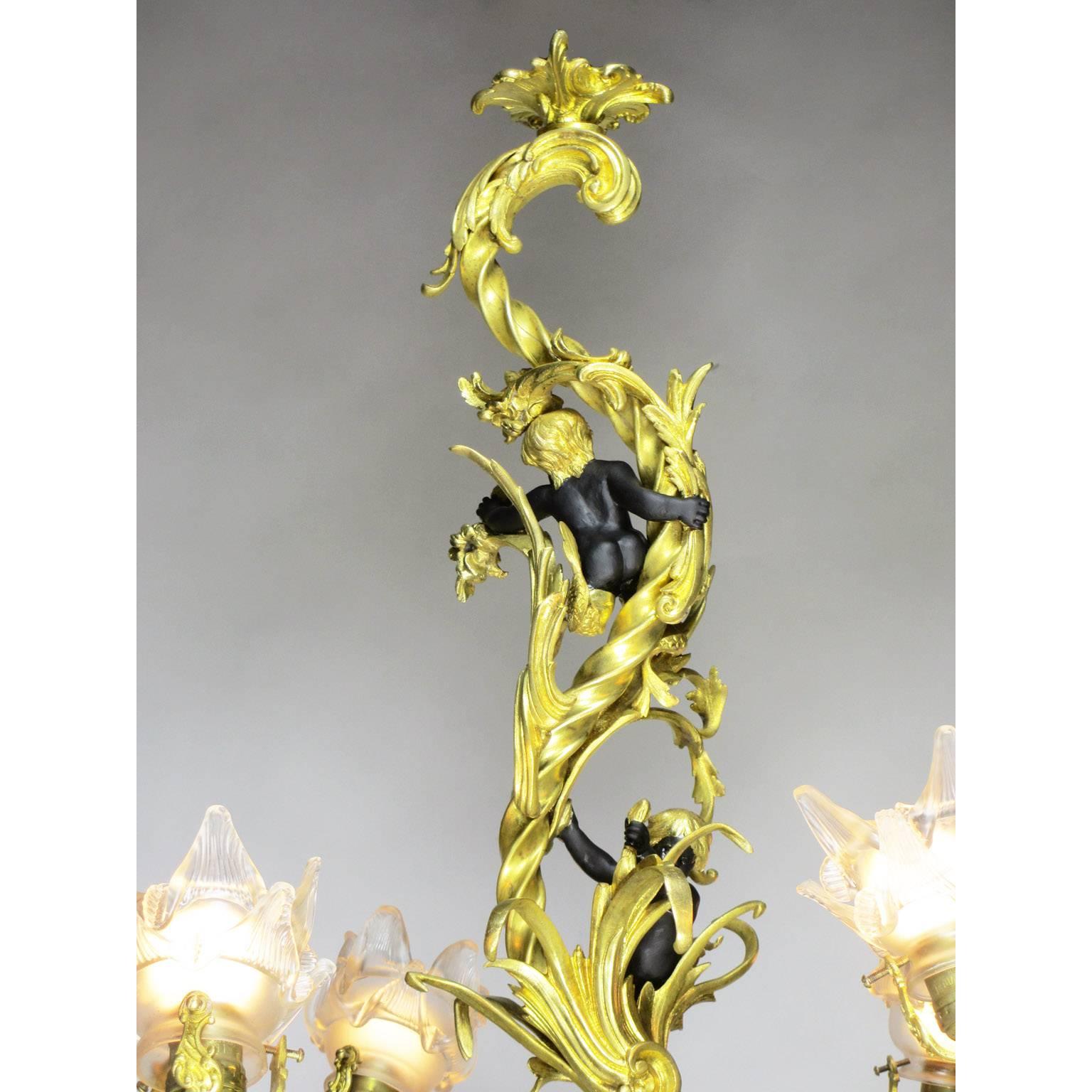 A fine French Belle Époque gilt and patinated bronze figural four-light whimsical chandelier. The scrolled gilt bronze body with branched arm lights with floral frosted glass shades, the upper stem surmounted with a pair of black-patinated bronze