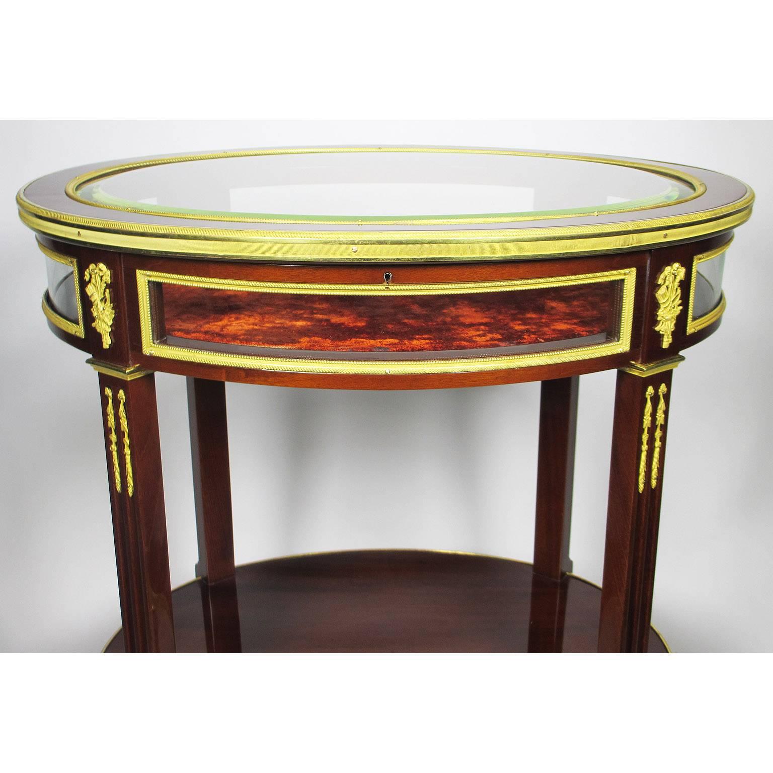 A fine French 19th-20th century Louis XVI style Belle Epoque ormolu-mounted mahogany Ovoid Vitrine table, in the manner of François Linke (1855-1946), with a beveled glass lift top and a lined interior, surmounted with gilt-bronze florets and arrow