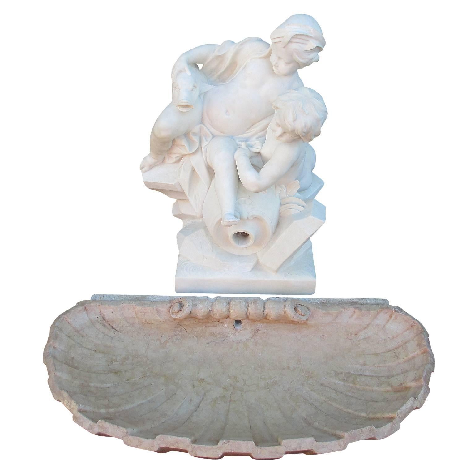 A fine and charming French 19th century carved white marble allegorical garden fountain group of two playful putti seated on a rocky outcrop with an upturned amphora supporting a stylized fish, drilled for water, together with a Rosso Verona marble