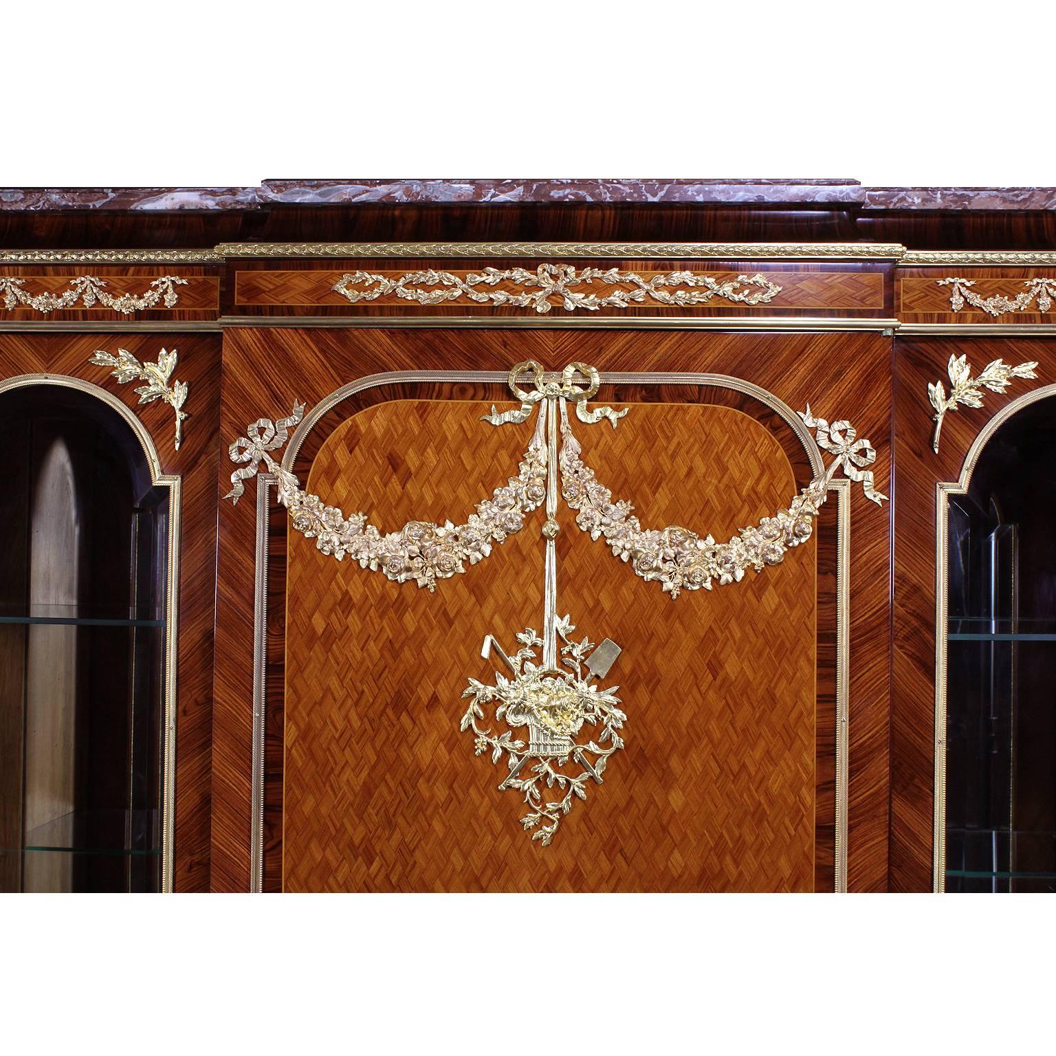 A very fine French 19th/20th century Louis XVI style mahogany, kingwood and tulipwood parquetry three-door vitrine with ormolu-mounted floral wreaths, ribbons, female masks and centred with an ormolu basket with flowers amongst foliage. The central