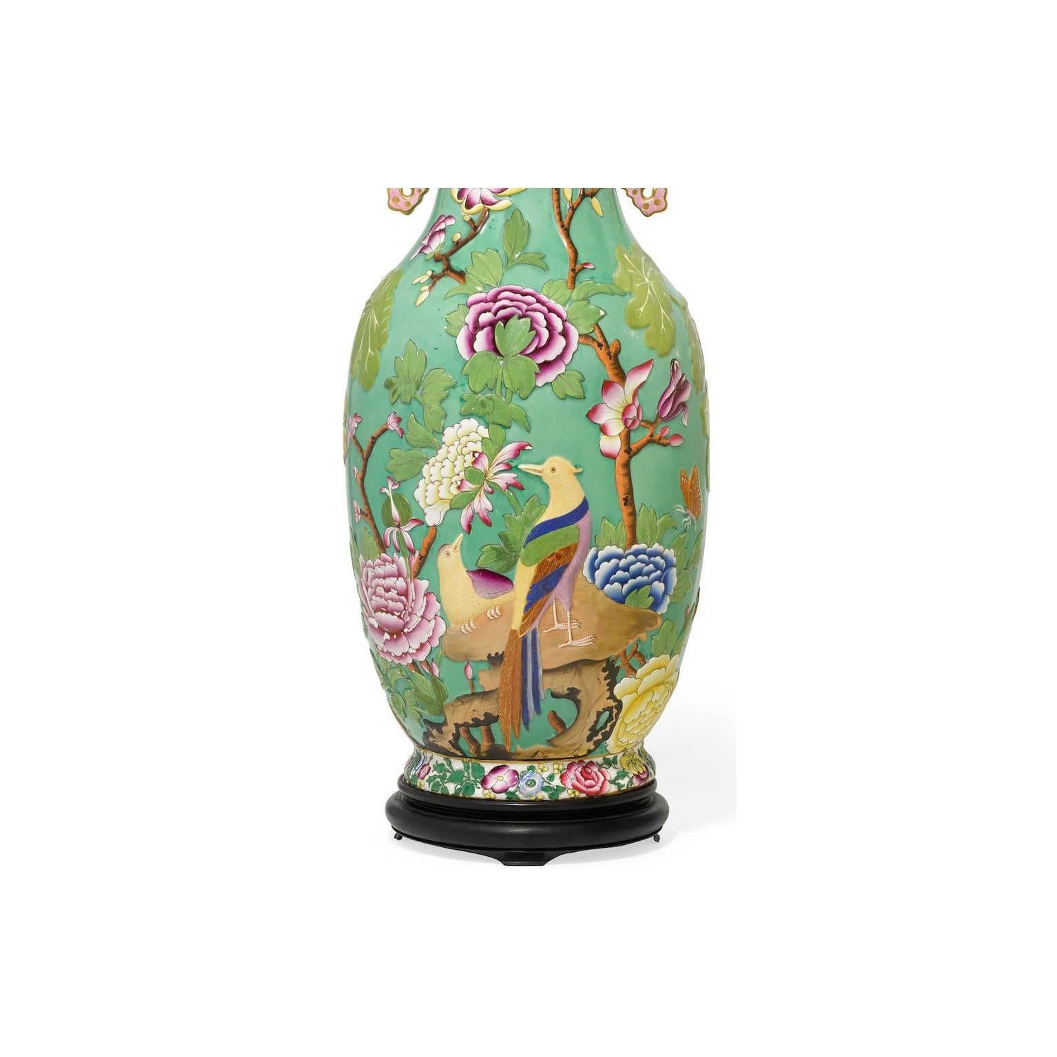 A fine and rare pair of English 19th-20th century chinoiserie style relief decorated porcelain vases, now converted into table lamps. The bright green enameled background decorated with colorful exotic tropical bird and raised on an ebonized wooden