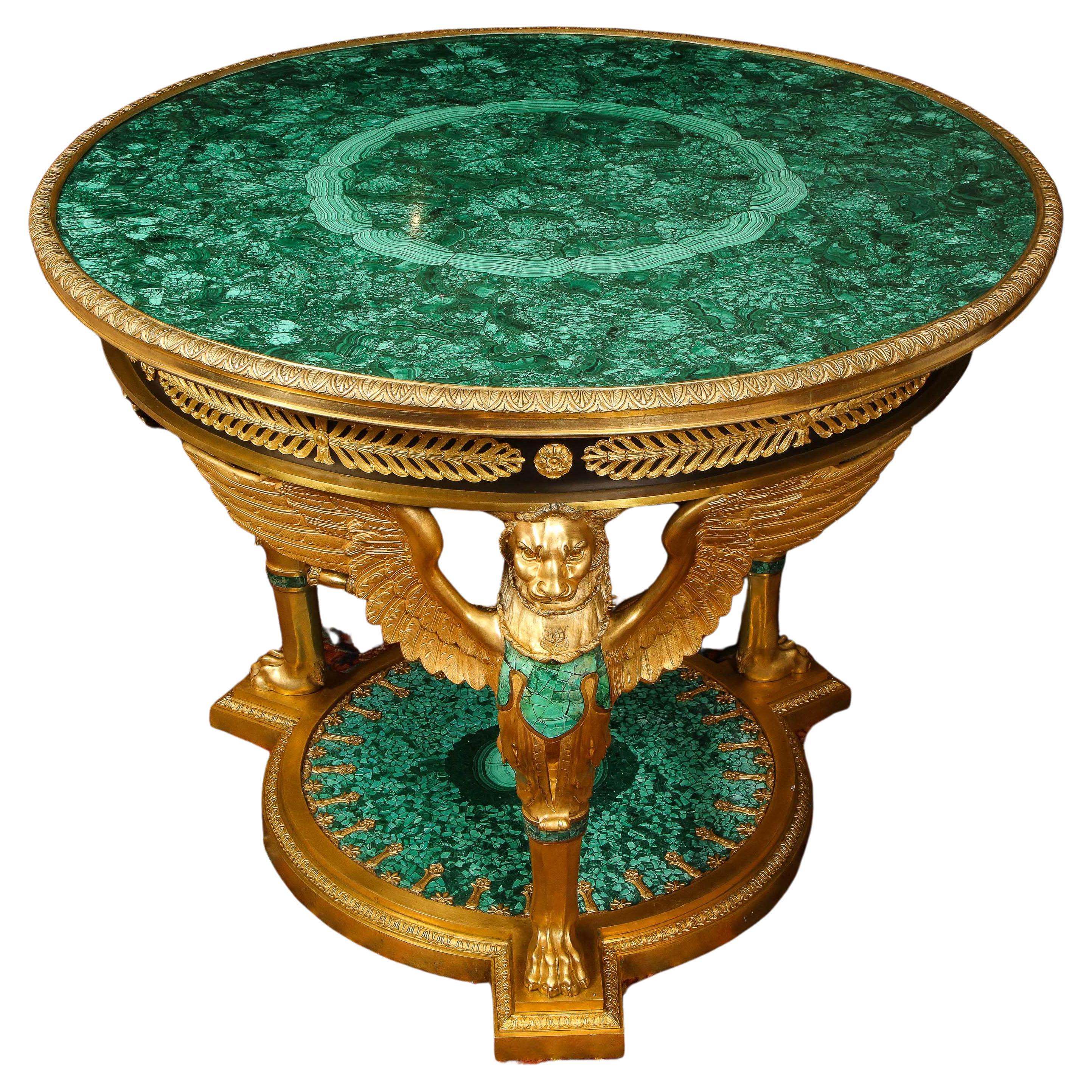 A large and impressive empire style ormolu and malachite center table

With a circular malachite-inset top with floral-cast bronze border rim, above a conforming frieze applied with alternating rosettes and anthemia, sitting on triple winged-lion
