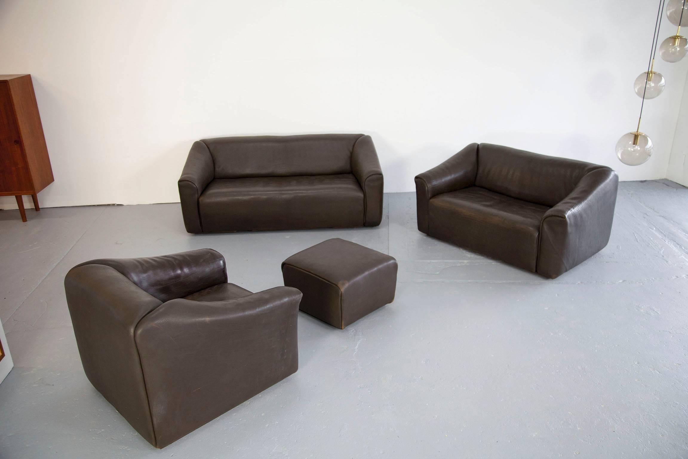 Great living room set manufactured by De Sede. The sofa suite DS-47. Three-seat, two-seat and matching lounge chair with ottoman. Covered with dark brown buffalo leather. 

Dimensions: 
Three-seat 90 x 180 x 70 cm/39 cm [D x W x H /