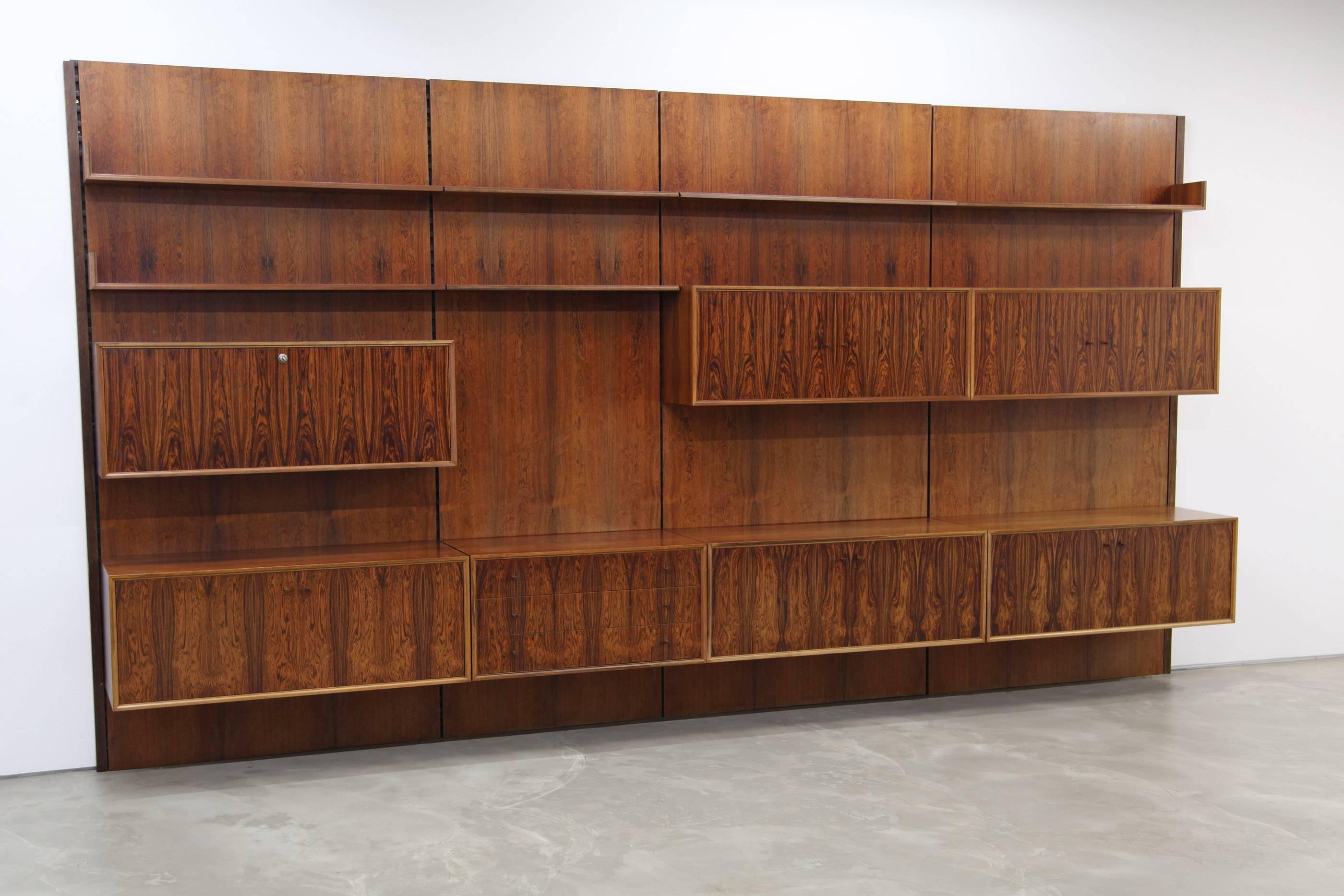 Very well made wall unit made with rosewood veneer by a German high quality manufacturer. This shelf features five cabinets, a bar cabinet and a chest of drawers as well as six shelves. It is in very good condition, the veneer shows some fading.