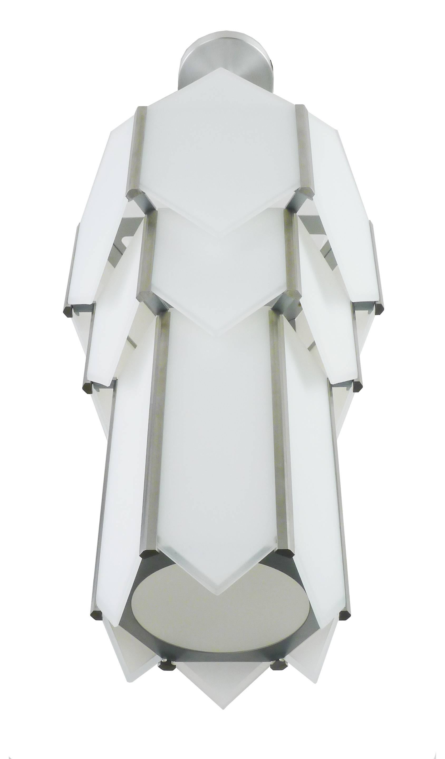 Stainless steel metal hexagonal chandelier with white glass panels. Glass panels have a 1/4 inch clear edge detail. Bottom has a circular opening with clear frosted glass. Incandescent lamping up to 100 watts.

Architect, Sandy Littman of Duesenberg