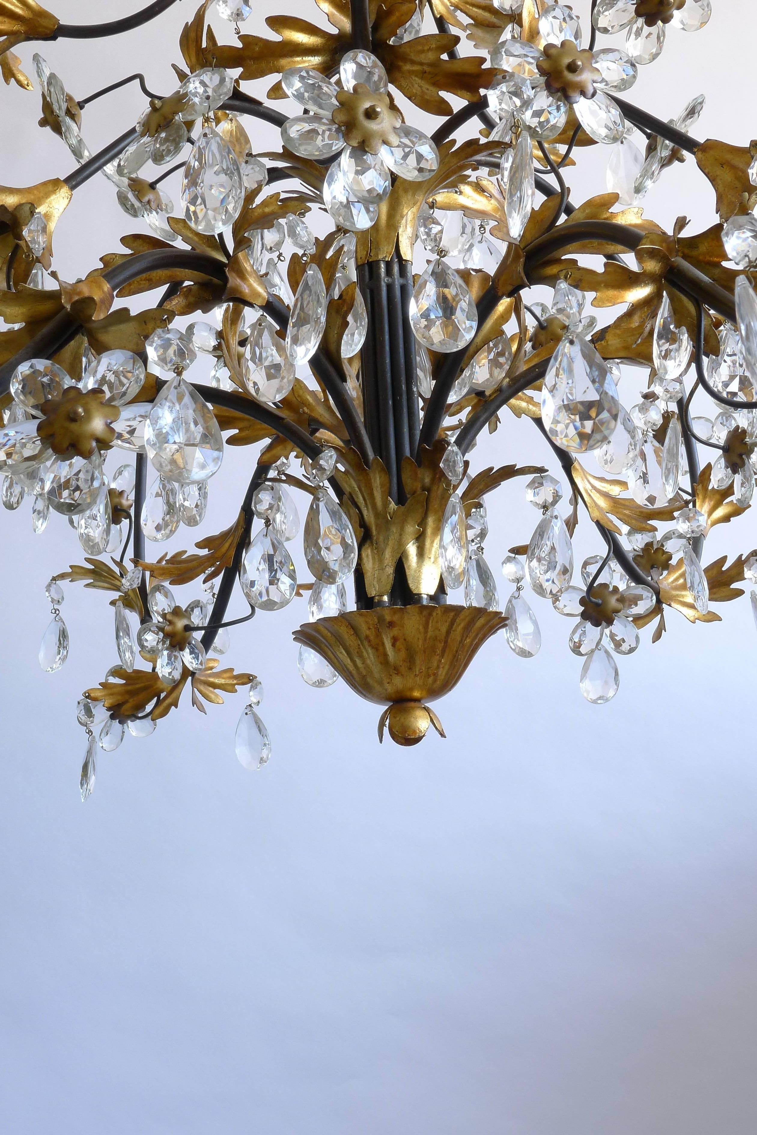 Wrought iron painted and gilt chandelier with fifteen arms. Crystal pentalogs and floral details. From the Hollywood Regency period. Incandescent lamping.

Architect, Sandy Littman of Duesenberg LTD.  and The American Glass Light Company have been