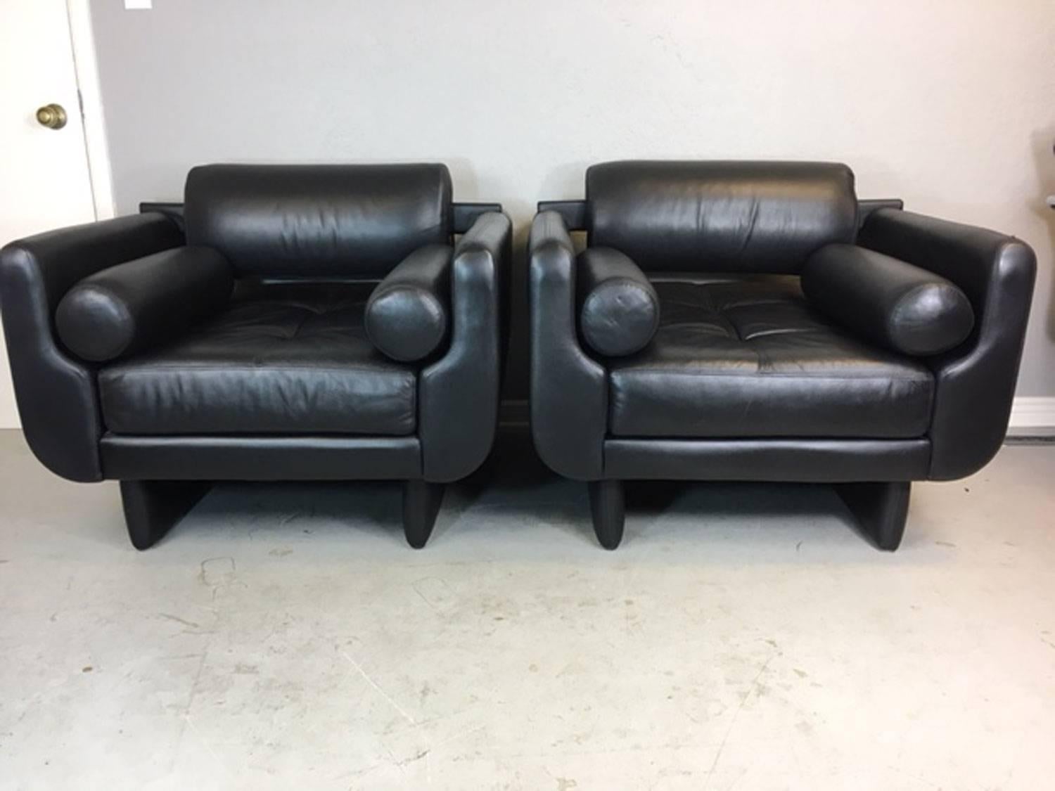 A pair of Vladimir Kagan Matinee club chairs by American Leather. A discontinued design that is reminiscent of an earlier Kagan club chair. These chairs also come with two red Tootsie roll throw pillows that may replace the existing black leather