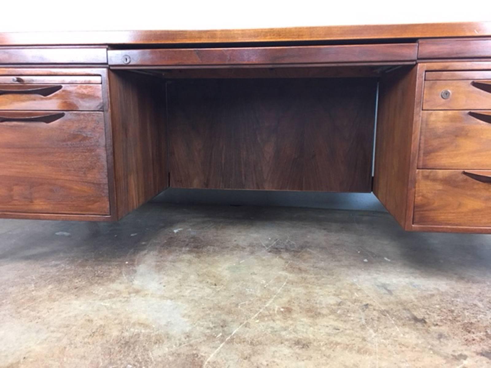 Stunning refurbished executive desk by Jens Risom. Handsome medium walnut. Large surface. Wood pull out working trays. Four drawers.