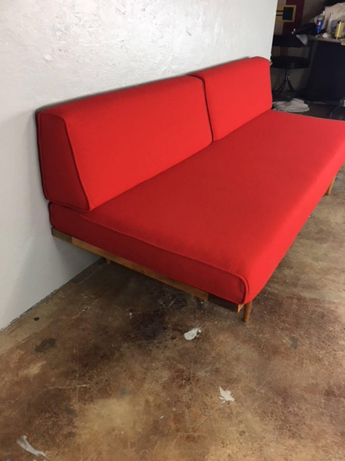 1960s Mid-Century Modern daybed in a red upholstered fabric. No rips, tears, or holes or unusual wear. This daybed was manufactured to be placed against a wall with the backrest cushions nestled directly against a wall. Easy transformation into a