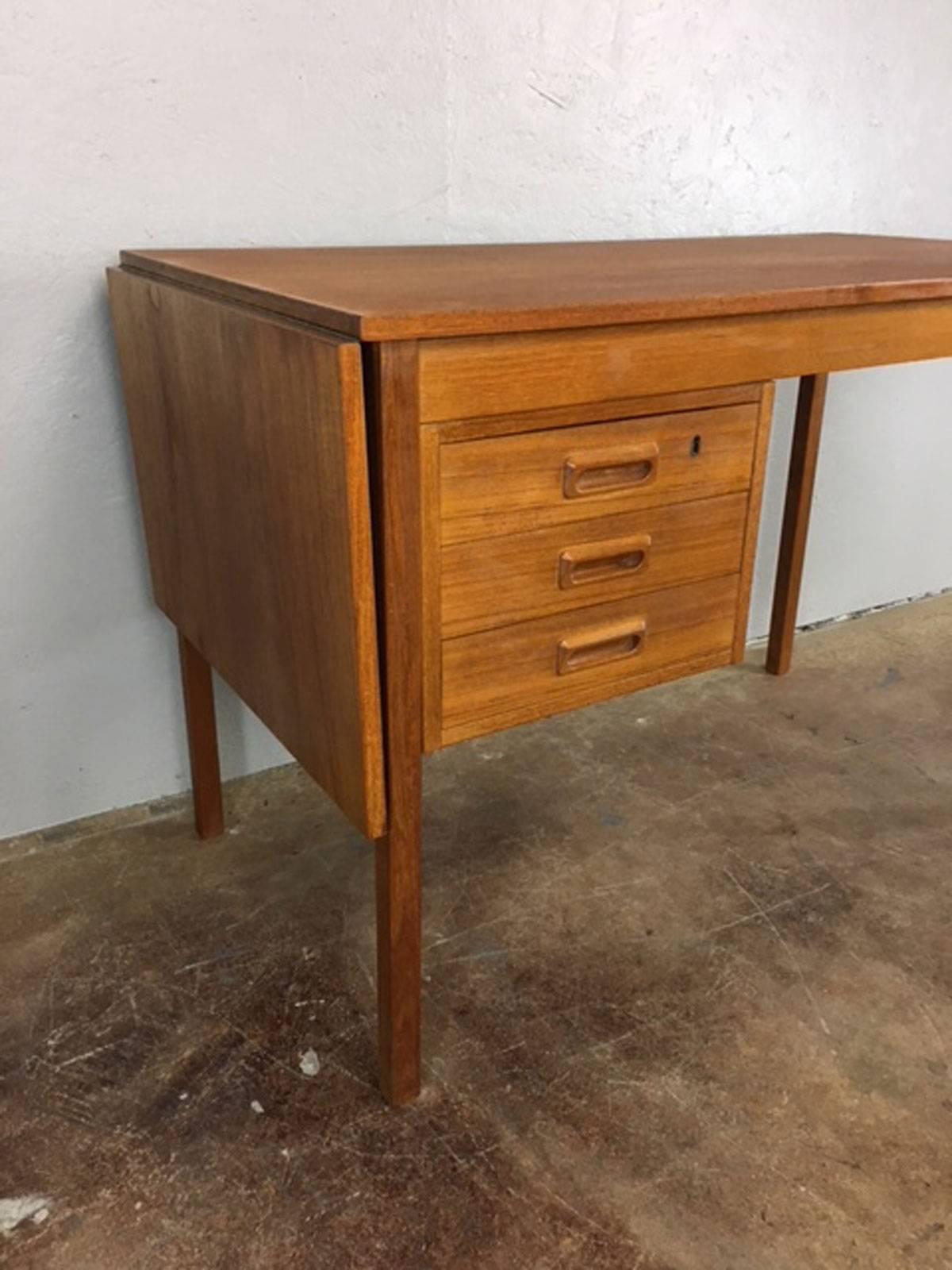 Unique drop-leaf desk in teak. Leaf folds up and then entire top slides into position to form one long top, if needed. Drawer locks. Nice clean piece. Measure: With leaf in down position this desk is 43 inches wide. 58 inches when leaf is in the