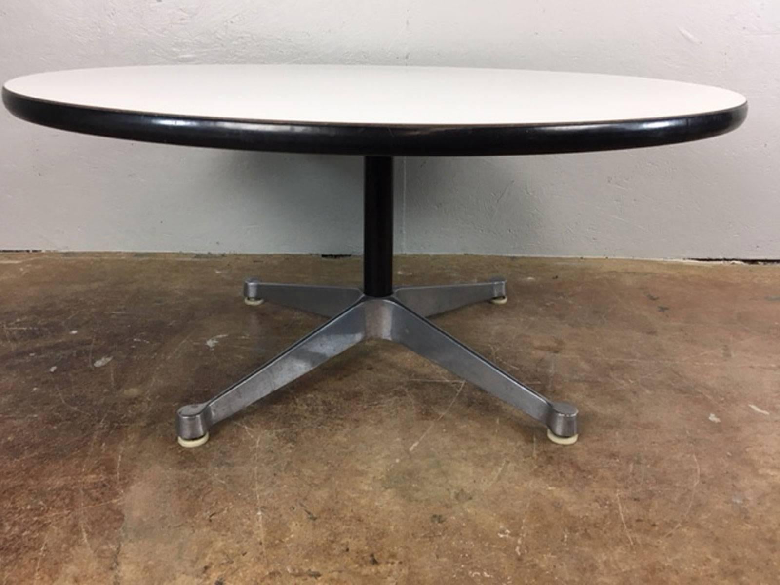 This 1960s Herman Miller Mid-Century Modern coffee table features a white formica surface with black trim, and steel pedestal legs.