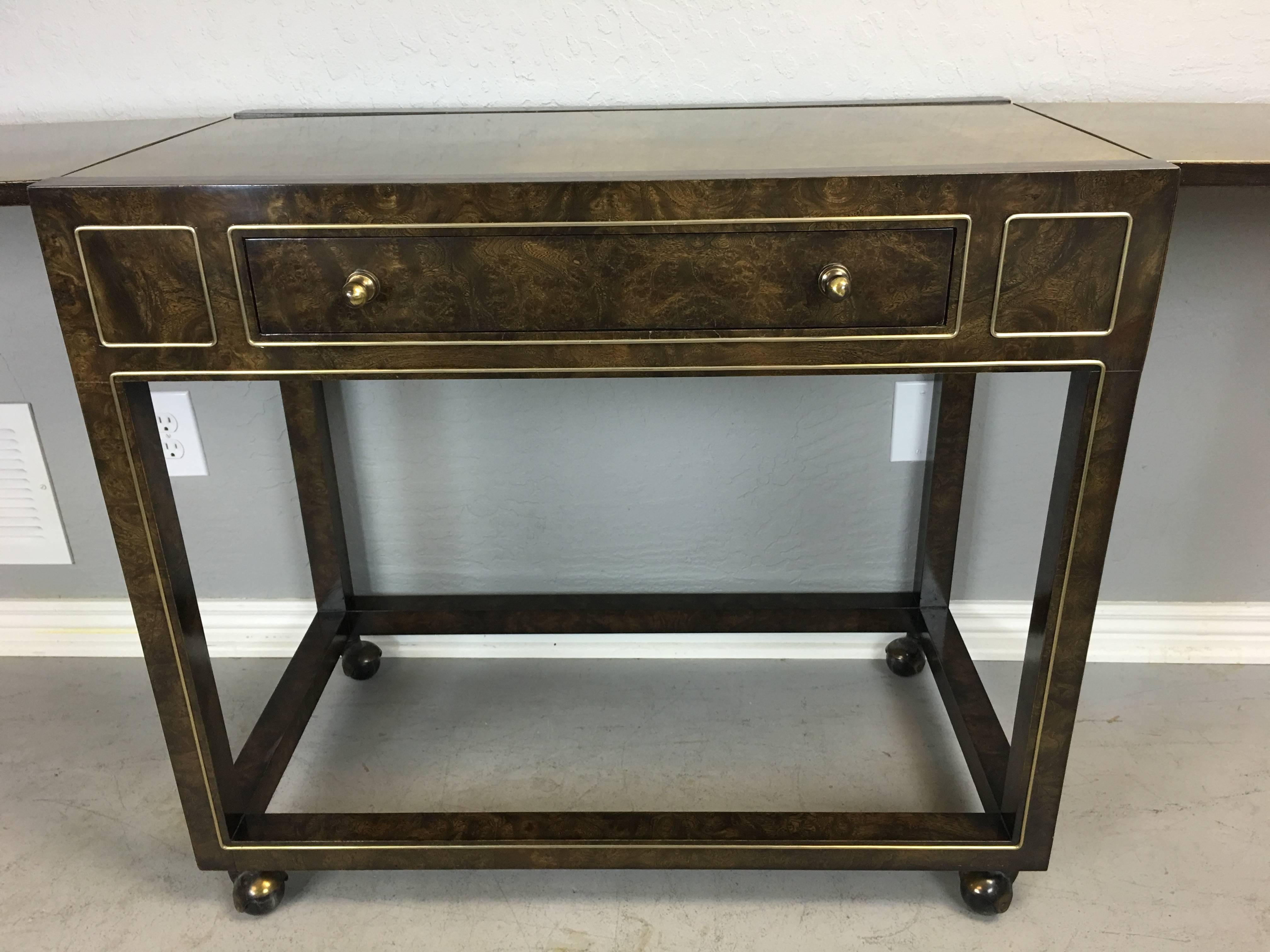 This is a serving or bar cart from the early seventies. Made by Mastercraft and boasts acid etched brass laminate top and Carpathian elm laminate with brass adornments. It can be extended to 76