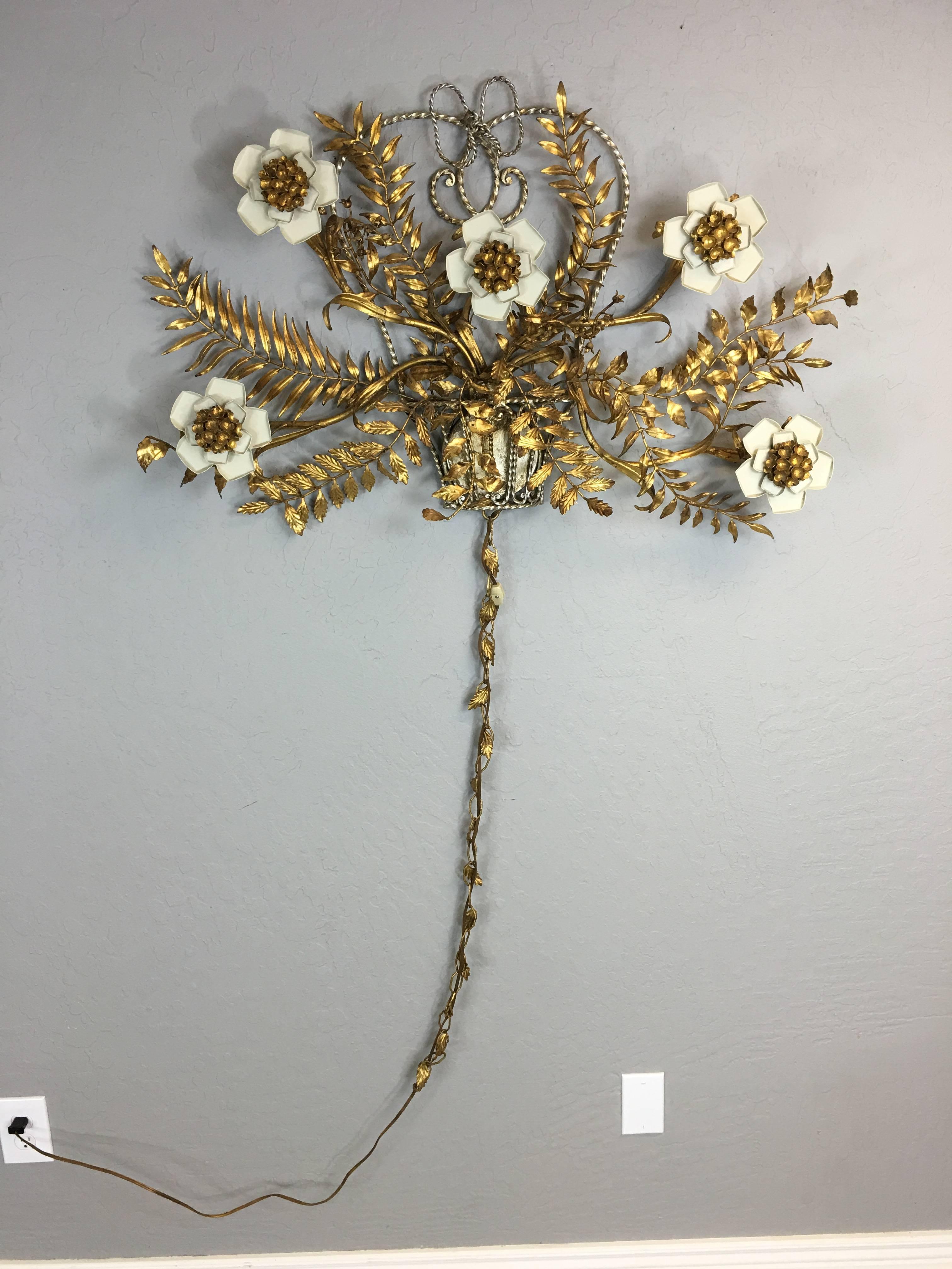 This piece is a gold colored lighted metal wall art in the Hollywood Regency style. It has branches and leaves and five metal flowers that light up, circa 1960. It measures 36' across x 24